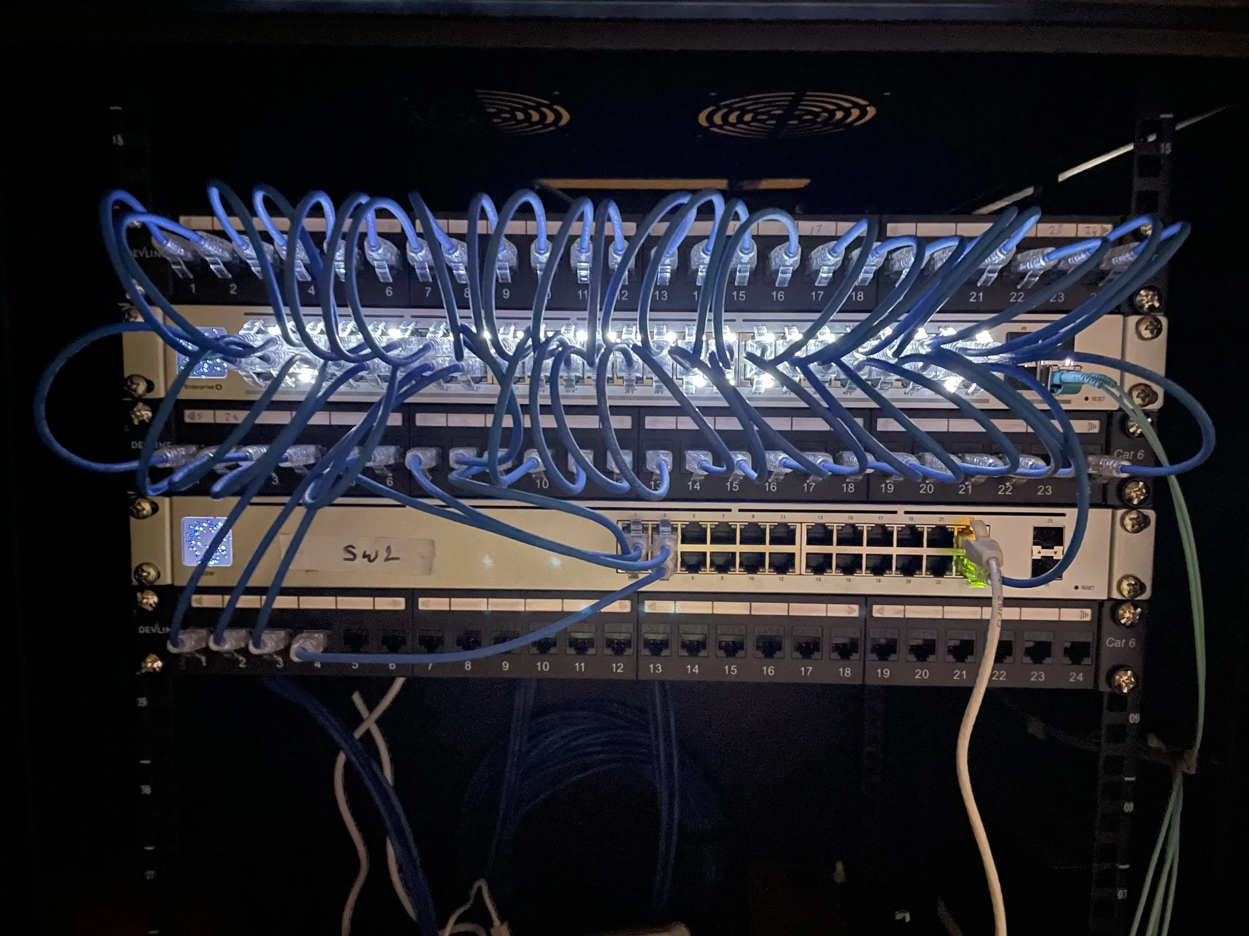 A network switch with multiple blue Ethernet cables plugged into various ports, illuminated by LED lights.