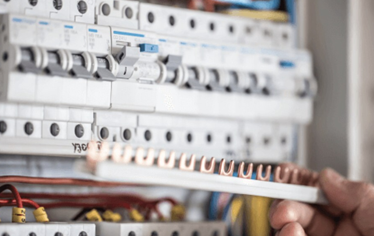Close-up of a hand adjusting a wire in an electrical breaker panel with multiple circuit breakers and wires.