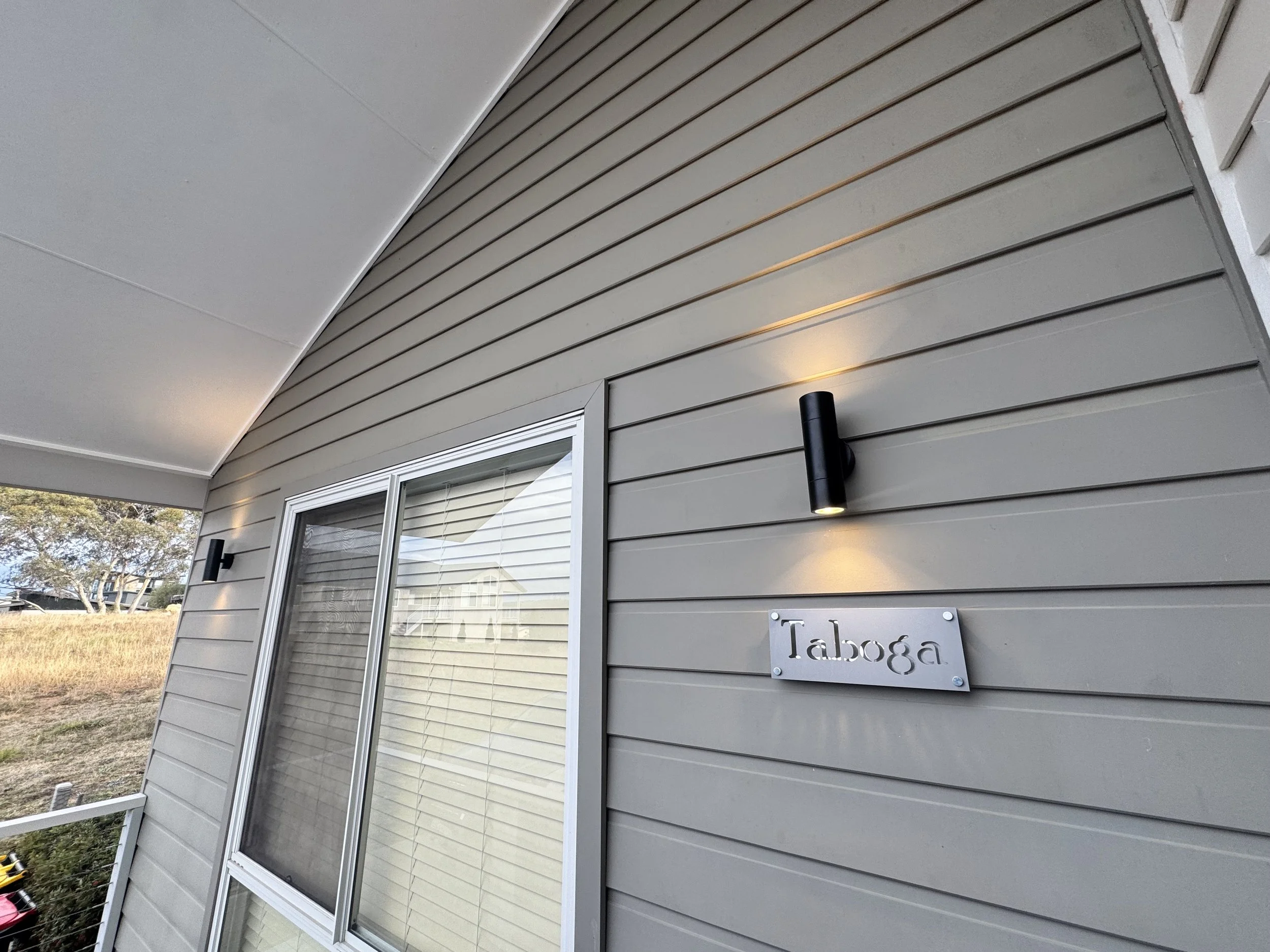 Close-up of a gray house exterior with horizontal siding, a sliding glass door with blinds, and a wall-mounted black outdoor light fixture.