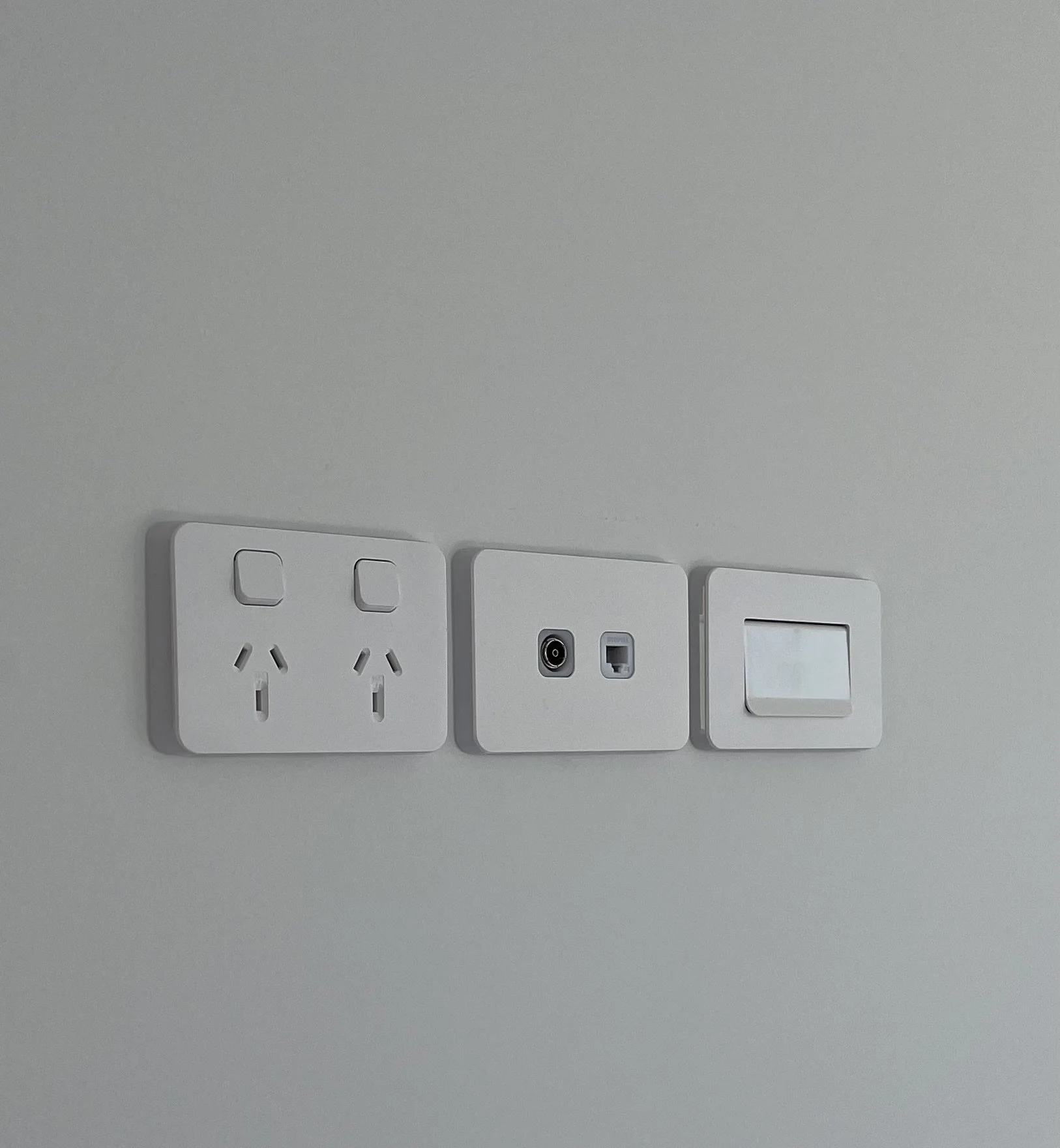 Close-up view of white electrical outlets, switches, and a power cord socket mounted on a gray wall.