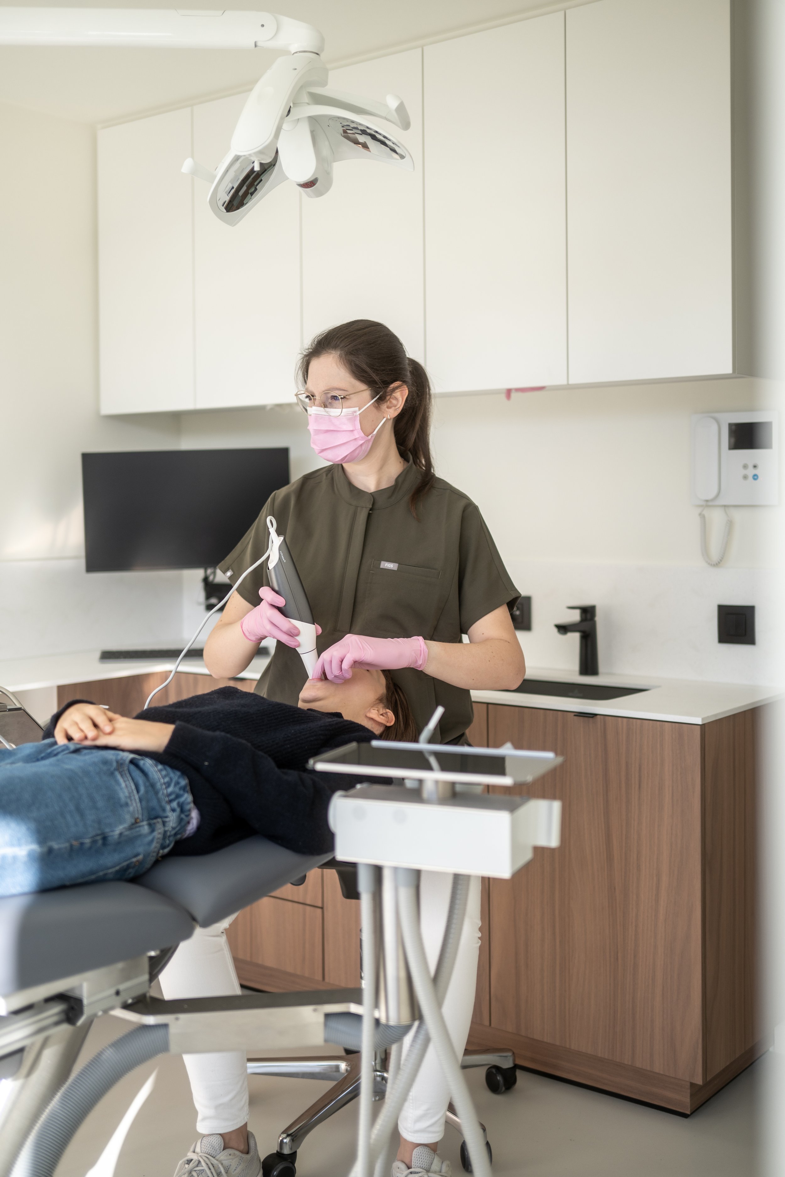 Tandarts of tandartsassistent in een kliniek met scrub en een mondkapje die een patiënt behandelt met een apparaat in de mond, liggend op de tandartsstoel.