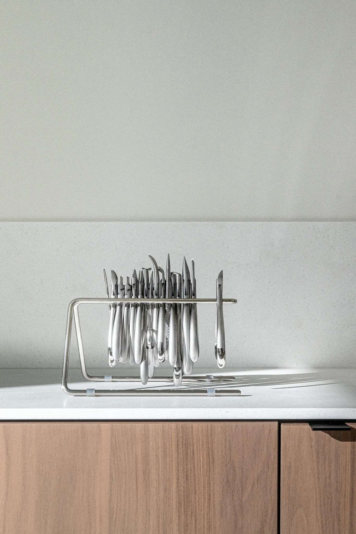 Een keukenlade met een roestvrijstalen bestekbak gevuld met messen, vorken en lepels, geplaatst op een witte keukentafel tegen een witte muur.