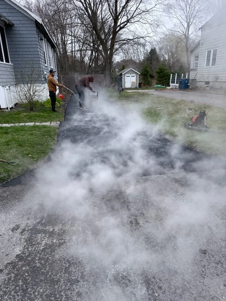 People pressure washing a driveway with steam and water, causing vapor and mist.