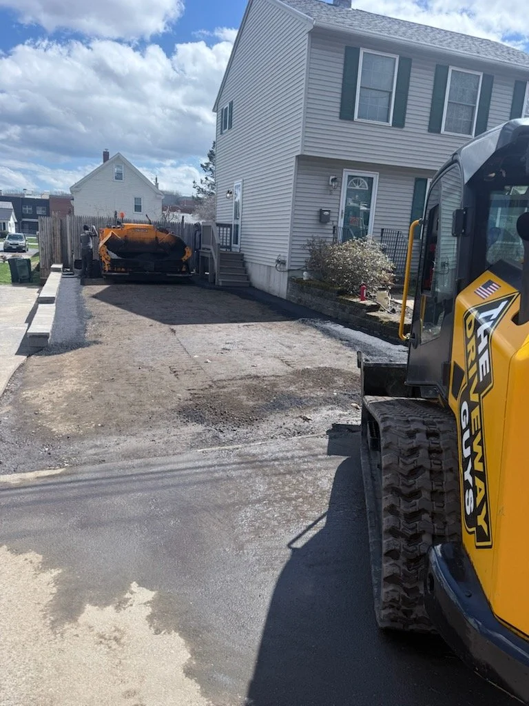 Construction equipment preparing a small driveway or parking area in front of a house.
