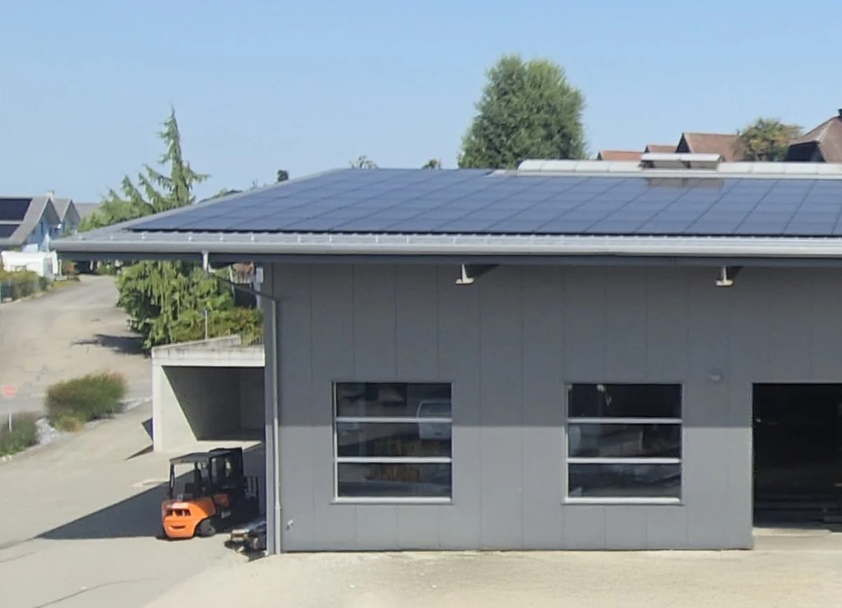 Ein Gebäude mit Solarpanels auf dem Dach und einem kleinen Fuhrpark vor dem Gebäude in einer ruhigen Wohngegend.