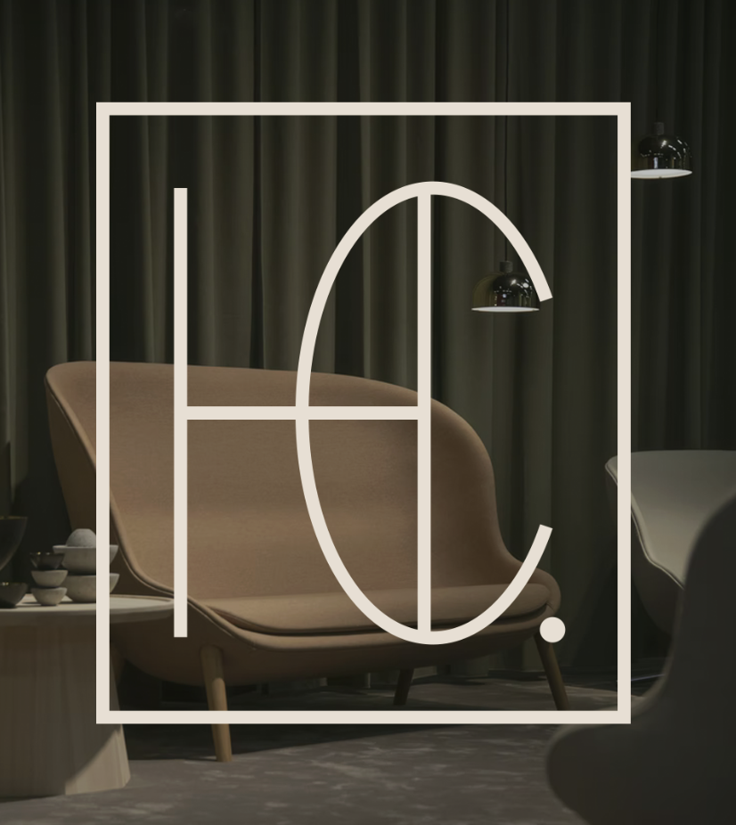 Intérieur moderne avec un fauteuil beige, rideaux sombres et lampes suspendues noires, avec un logo blanc en forme de ligne et de cercle superposé.