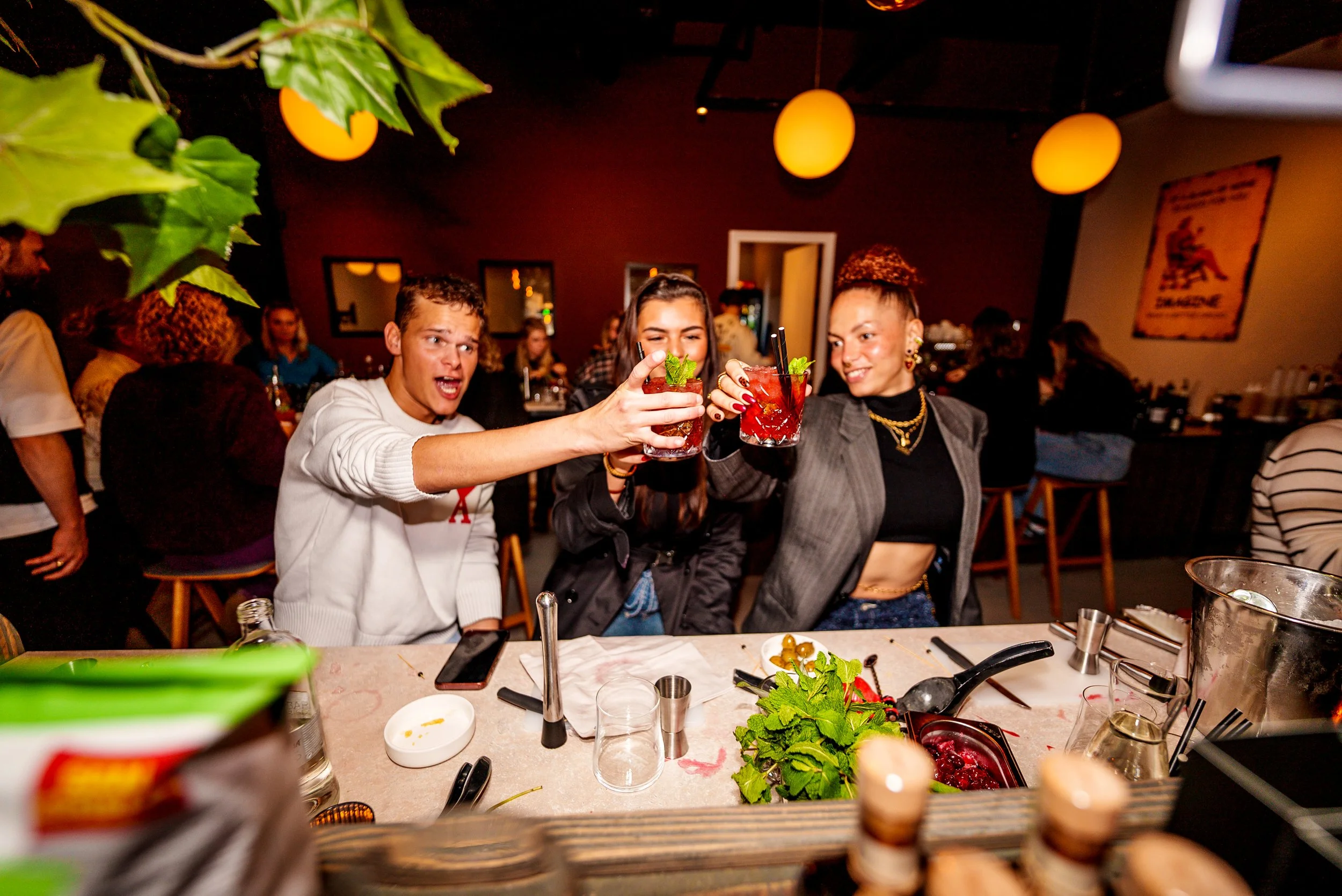 Drie mensen proosten met cocktails in een restaurant of bar, omringd door eten en gezellige sfeer van Barstories.