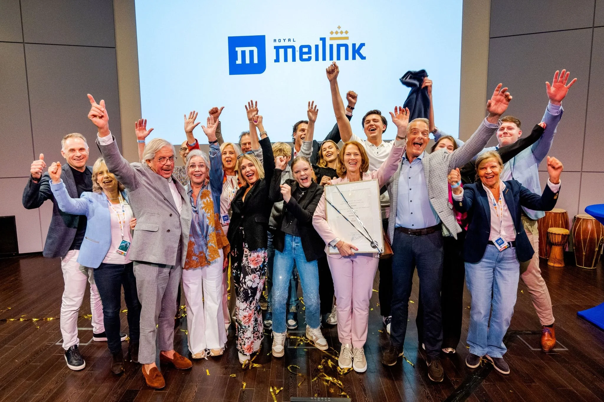 Een groep mensen die vieren op een podium met het logo van Melink op de achtergrond.