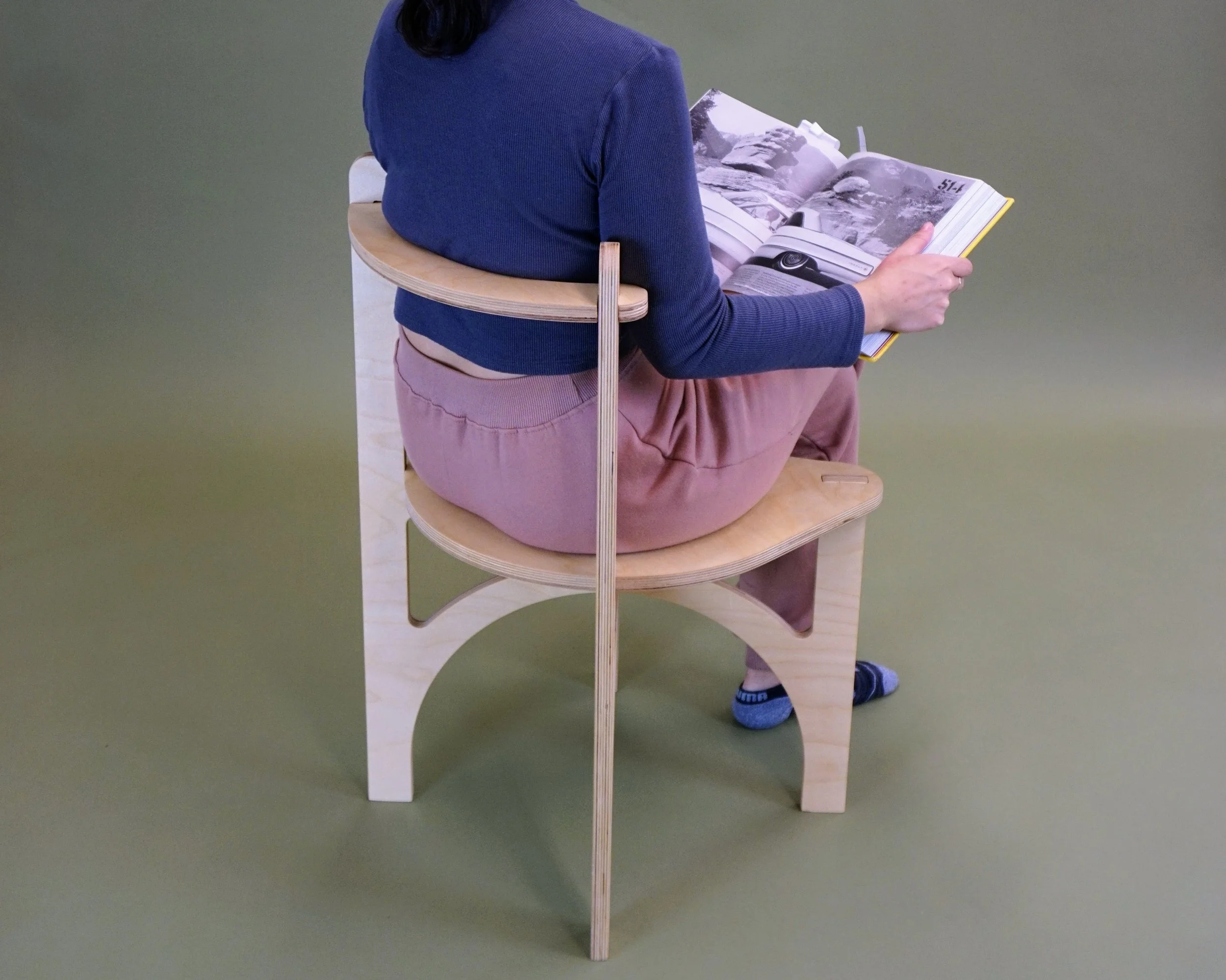 Person sitting in chair facing away from the camera holding a book open in their lap