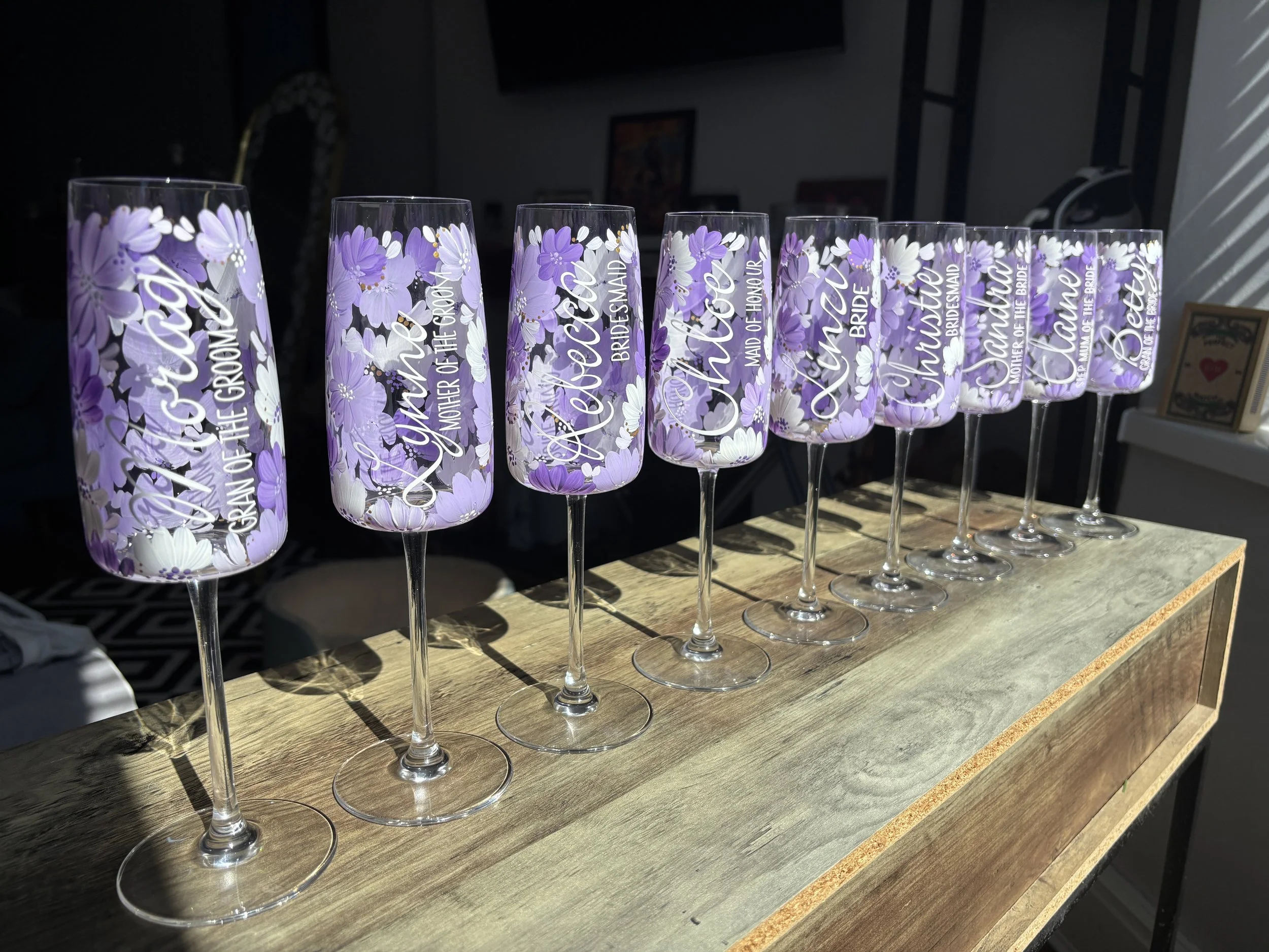 Set of wedding champagne flutes with purple and white floral designs, and various names in white text.