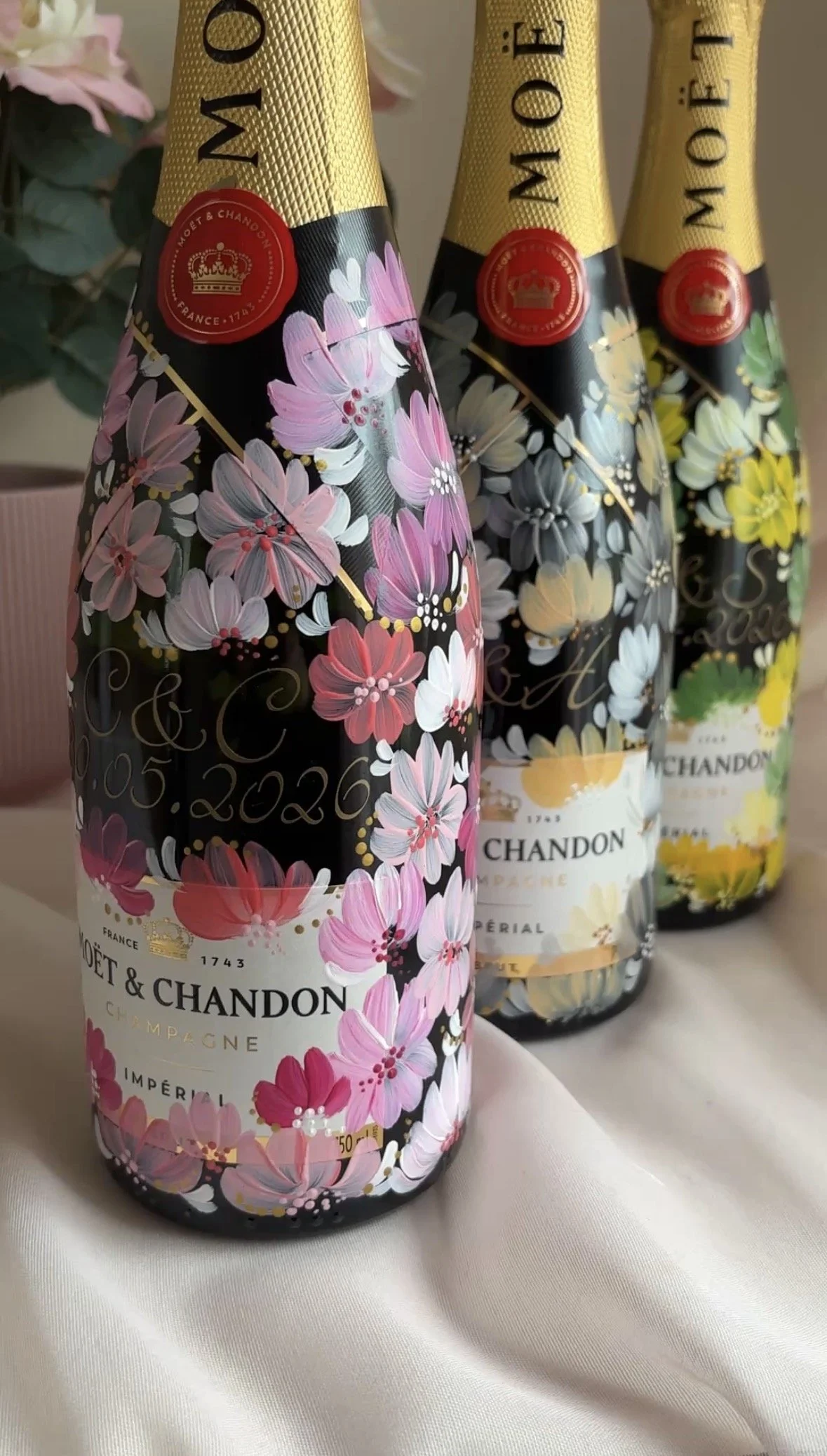 Three Moët & Chandon champagne bottles with hand painted floral designs on each of them in various colours like pink, cream, and blue.