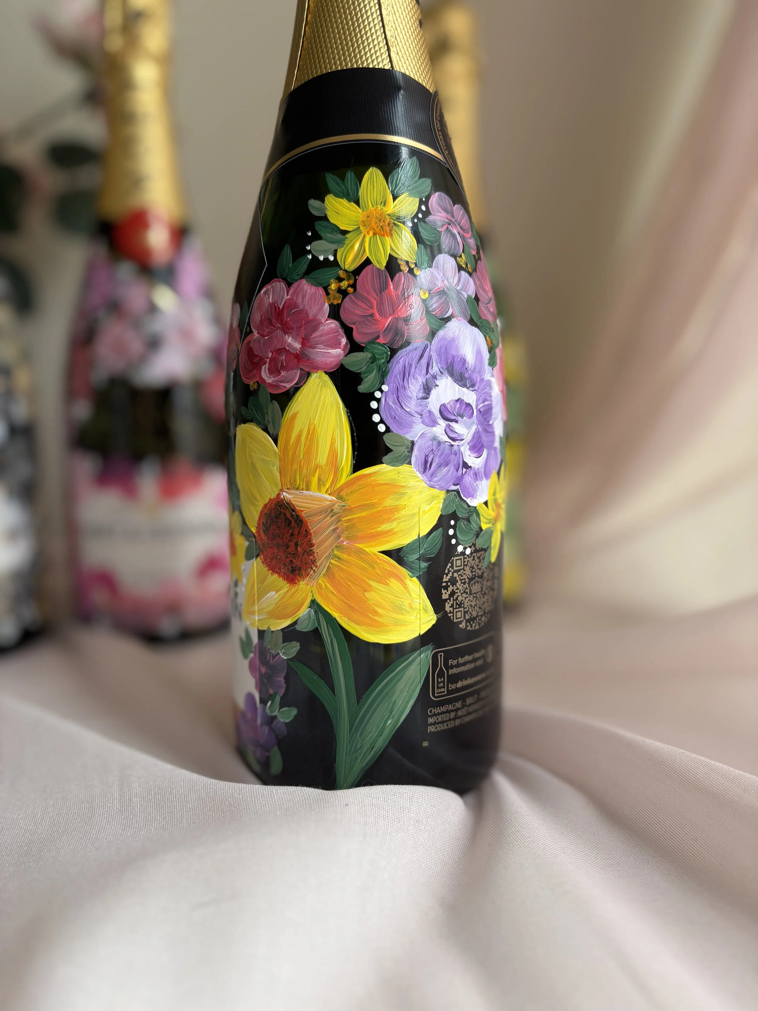 Close-up of a bottle with a floral painted design featuring sunflowers, and other purple, pink, and red flowers with green leaves.