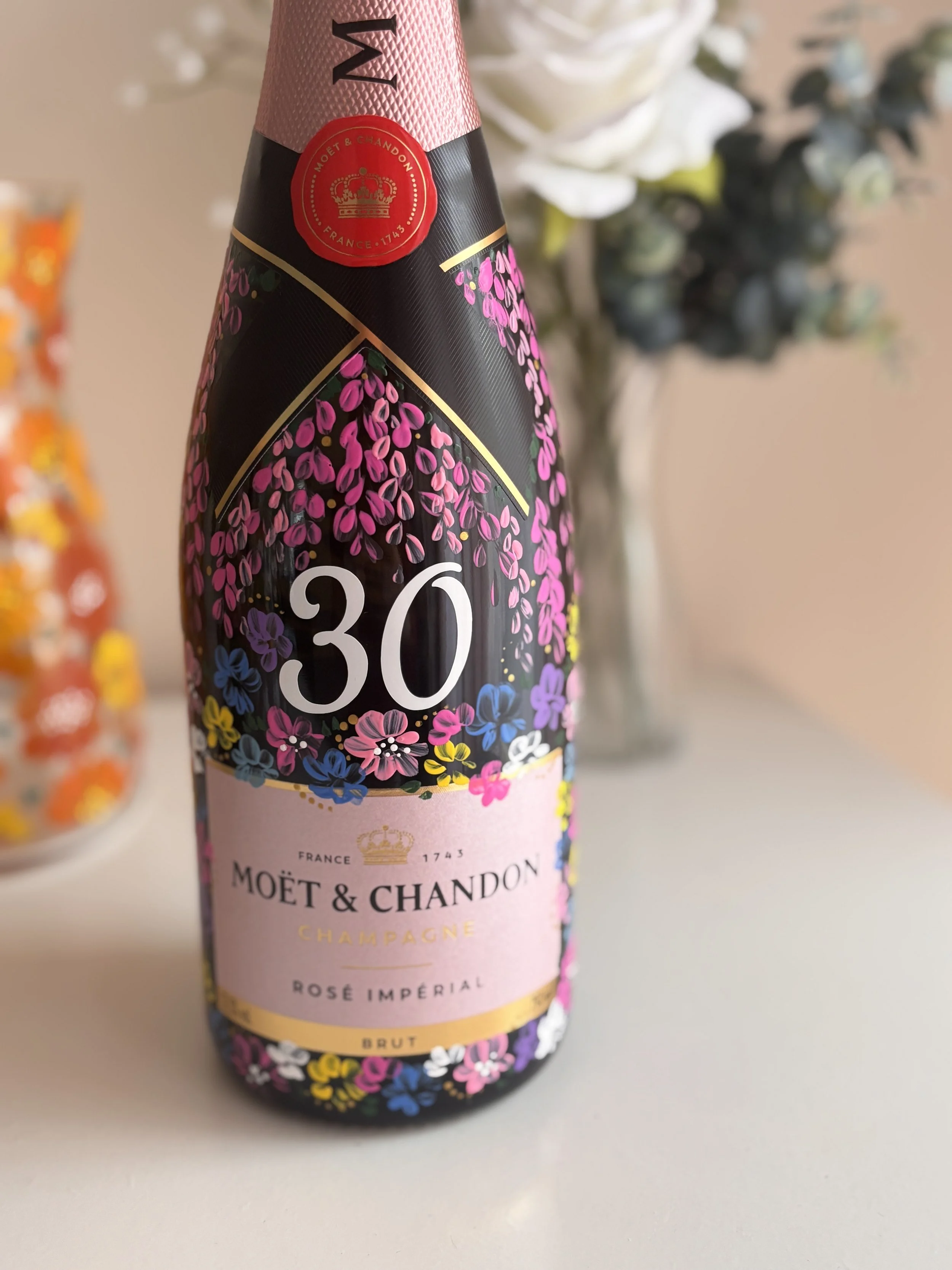 A bottle of Moët & Chandon Rosé Imperial Champagne with a pink label and floral design, and a blurred background of flowers.