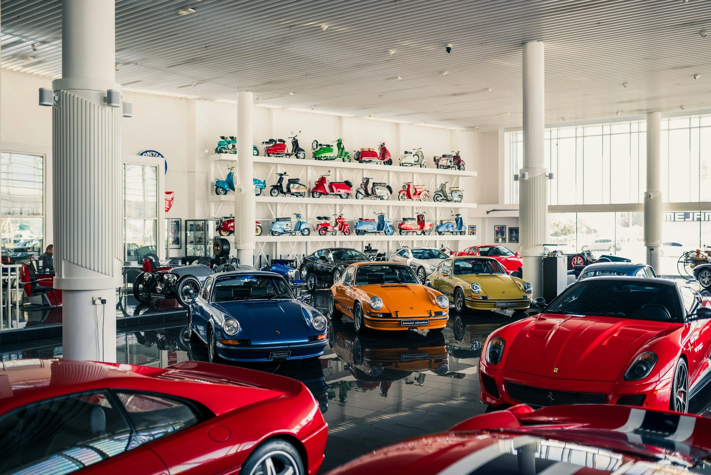 Innenansicht eines Autoshops mit mehreren rot, blau und gelb lackierten Sportwagen sowie einer Wand mit Modellmotorrädern in verschiedenen Farben.