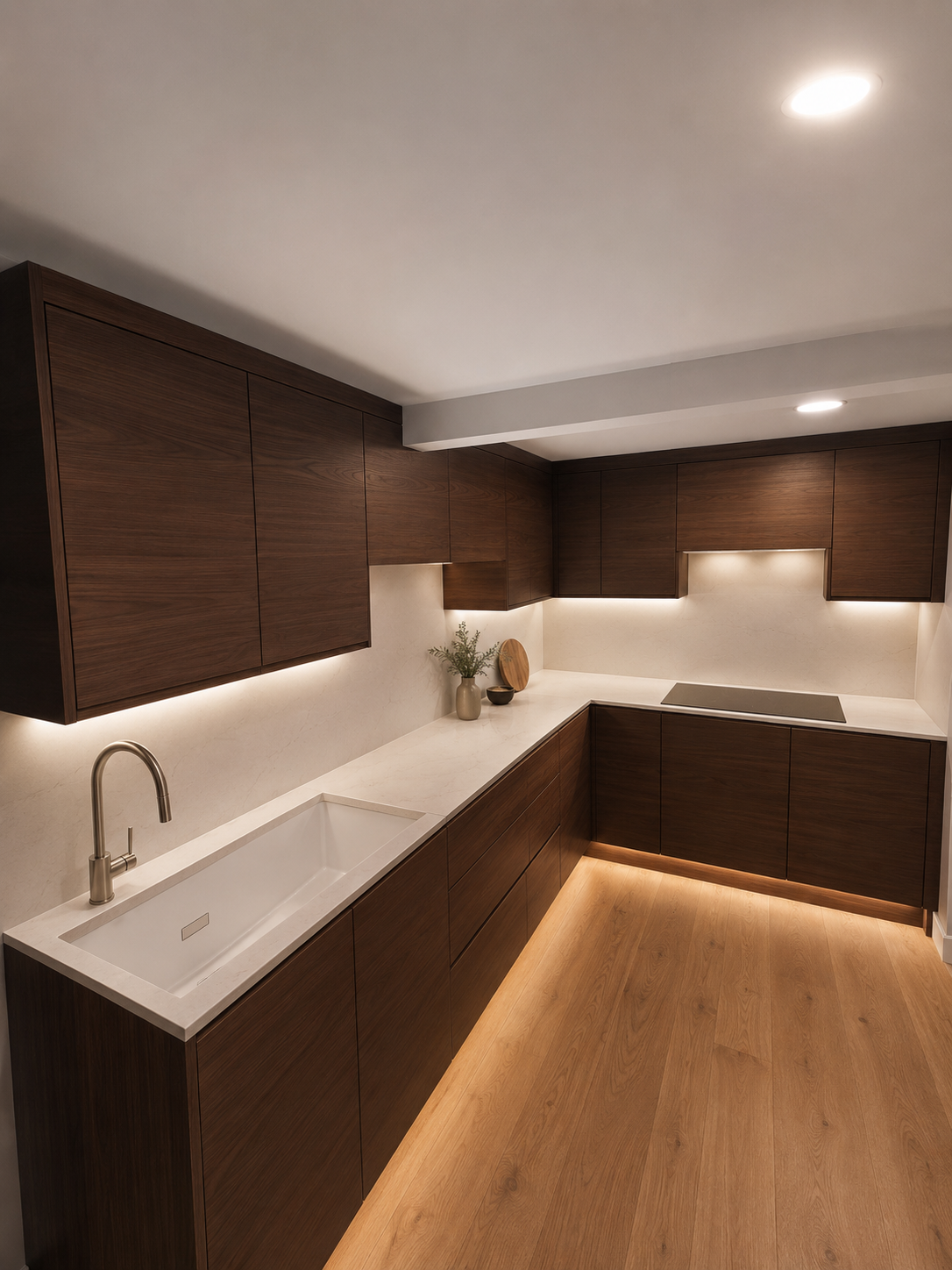 Modern kitchen with dark wooden cabinets, white countertop, built-in sink, and minimal decor, illuminated by ceiling lights and under-cabinet lighting.