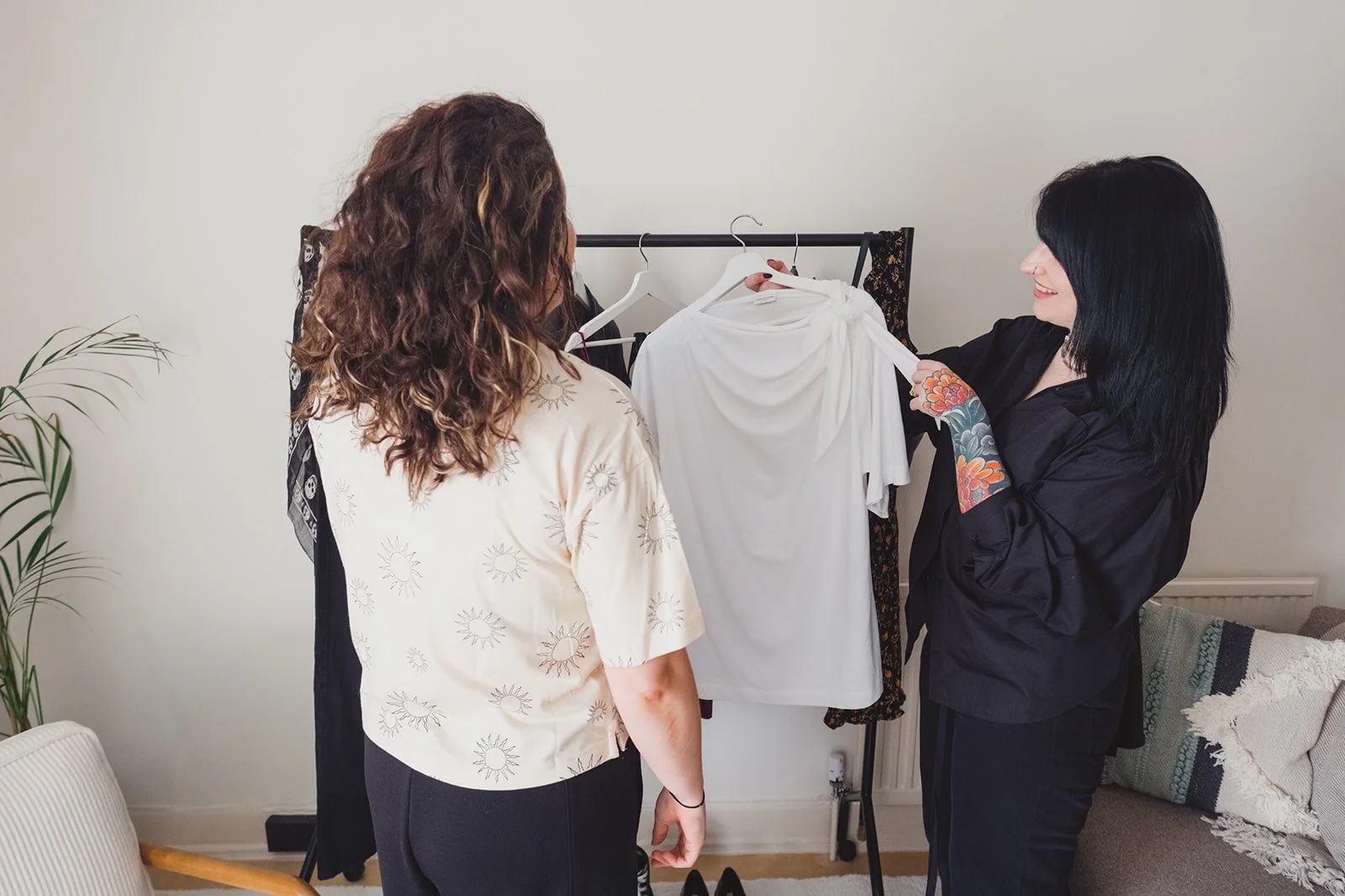 Two women choosing clothes from a garment rack, with one holding up a white shirt