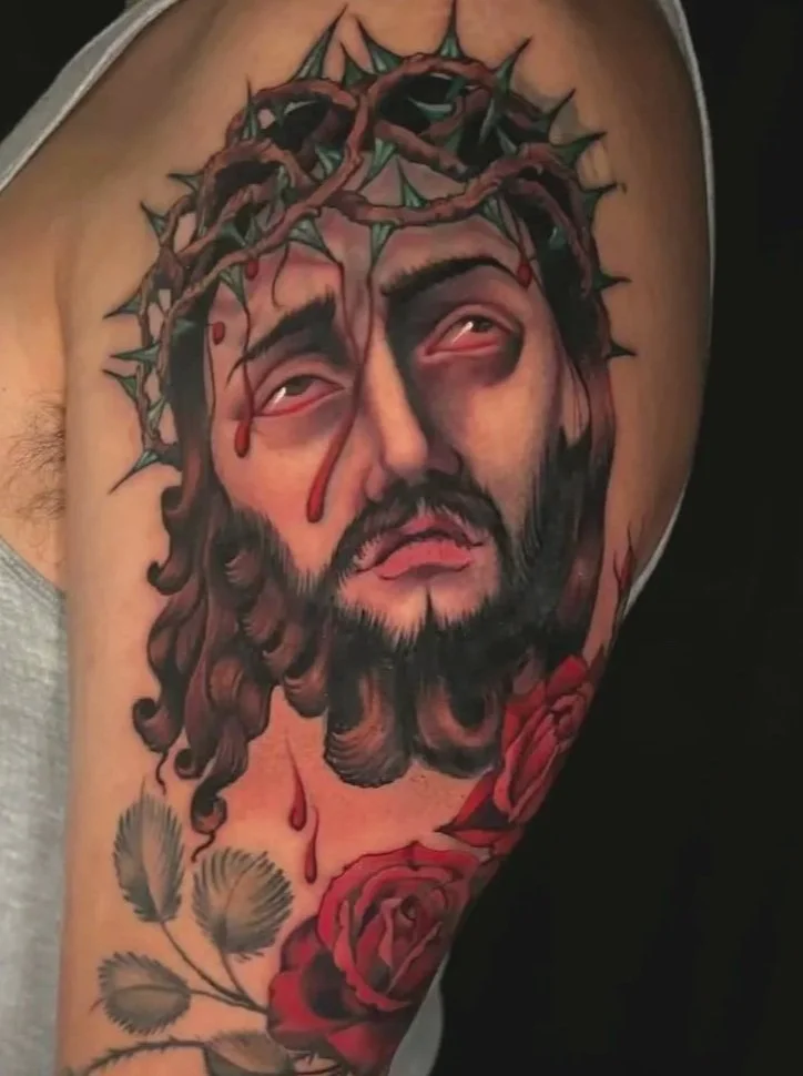 A tattoo of Jesus Christ with a crown of thorns, tears of blood on his face, and a red rose below.