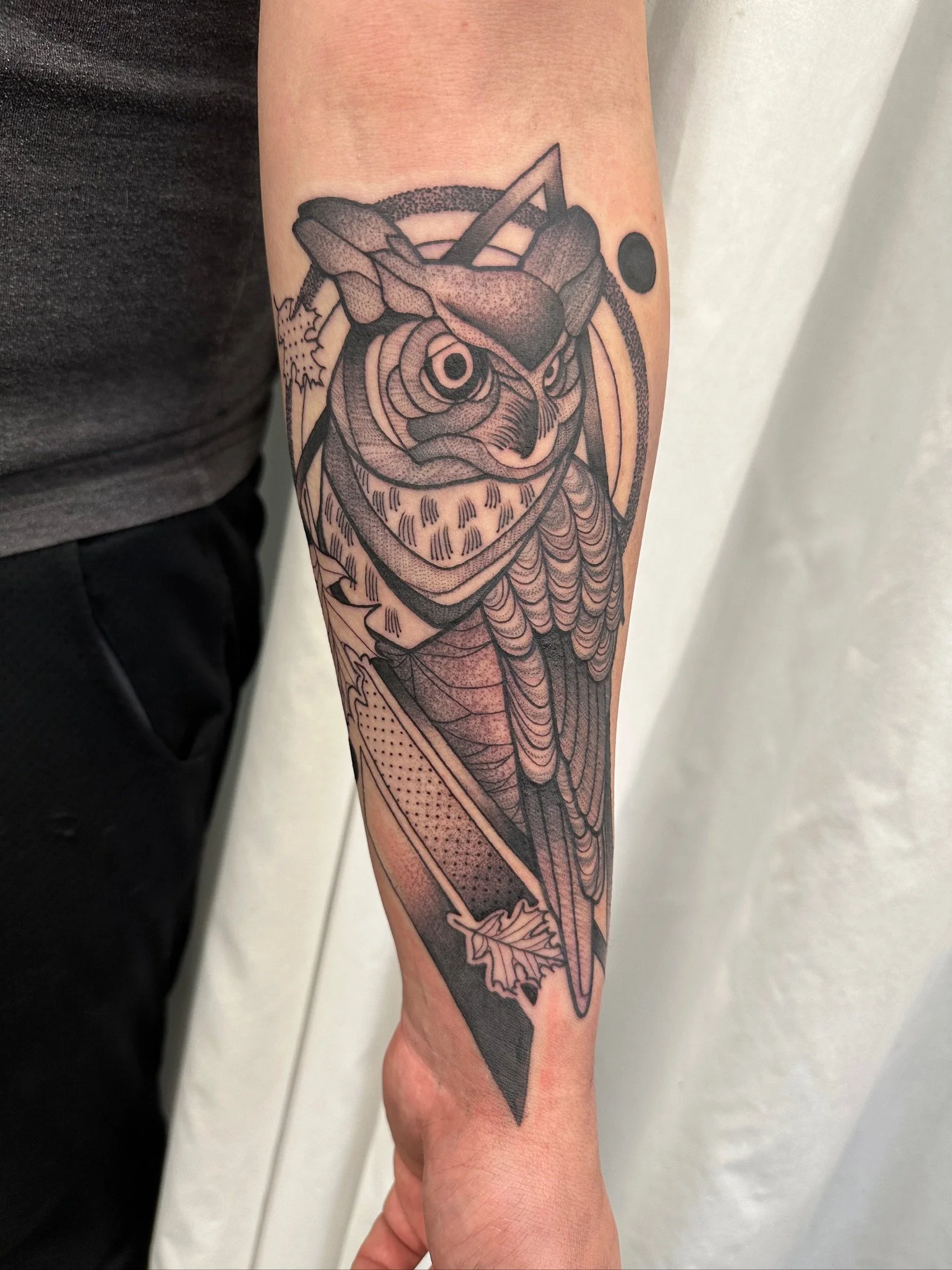 Black ink tattoo of a cicada on a person's forearm, featuring intricate line work and dot shading, with a background circle and a small black dot nearby.