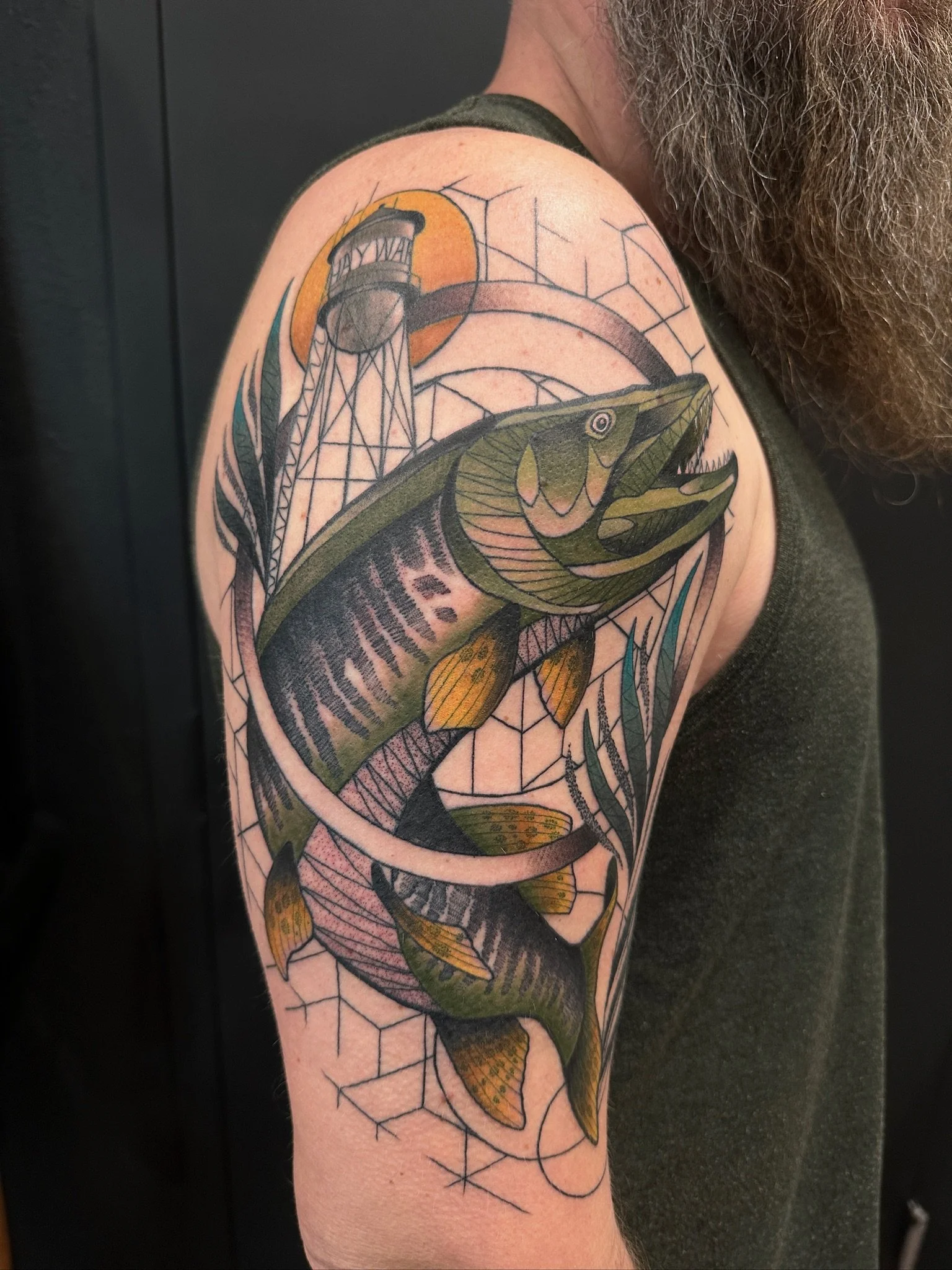 Tattoo of a fish with an orange background and a lighthouse in a geometric design on a person's upper arm.
