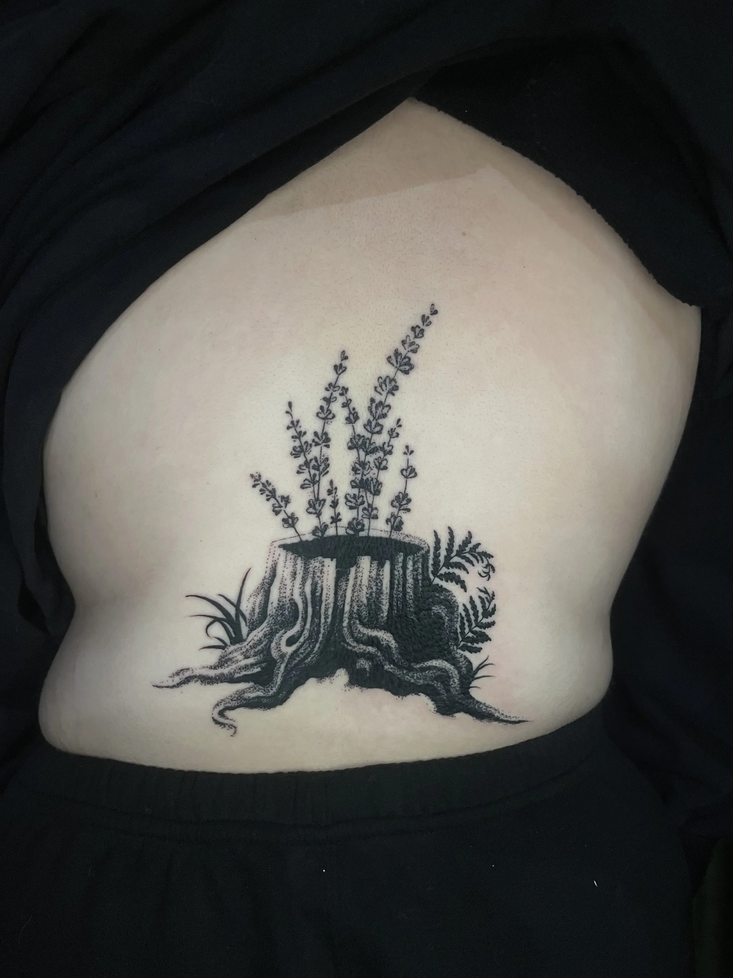 Tattoo of a tree with roots and branches, with the roots extending beneath and the branches reaching up.
