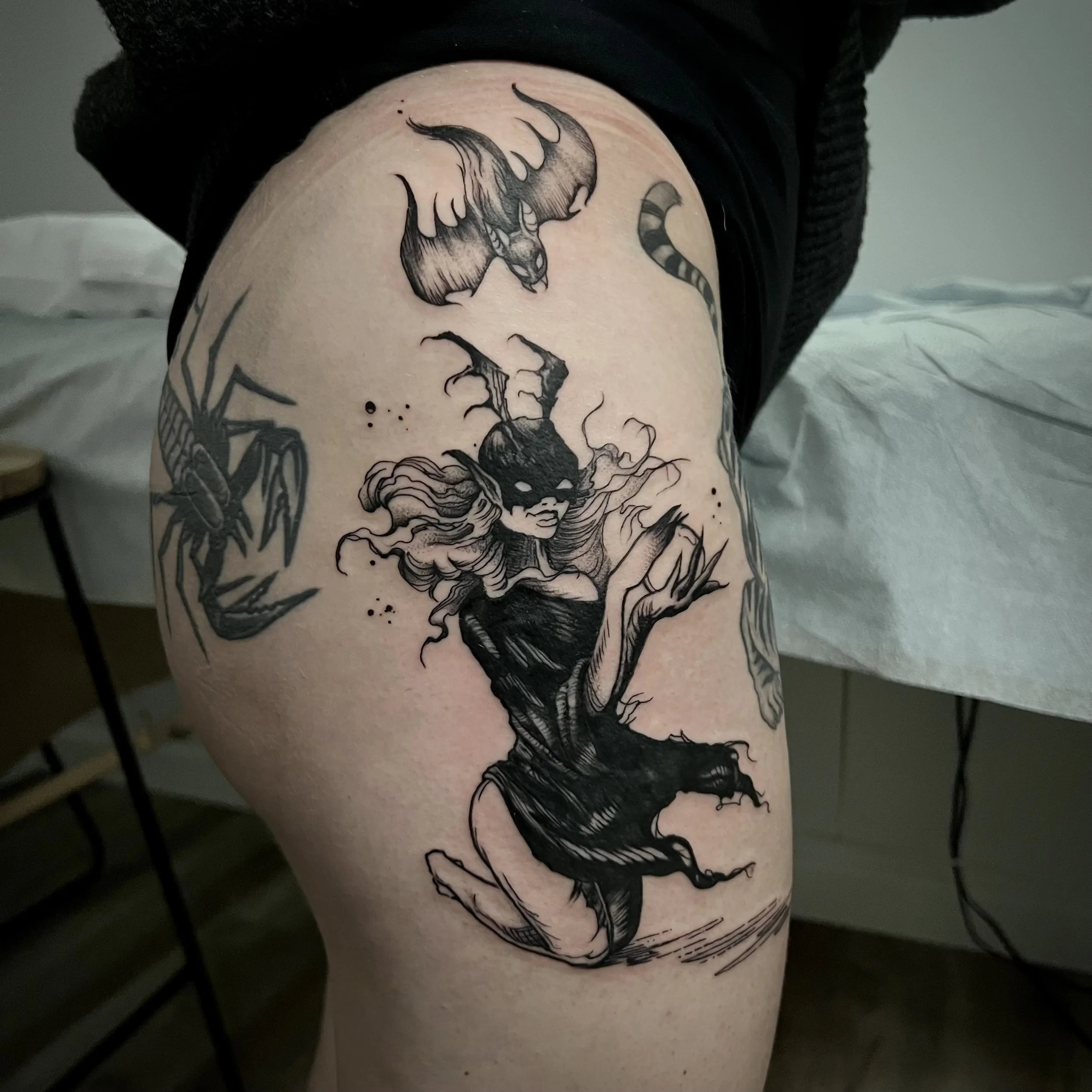 Black tattoo of a wild, fierce animal, possibly a wolf or a dragon, with detailed shading and sharp features, on a person's upper thigh.