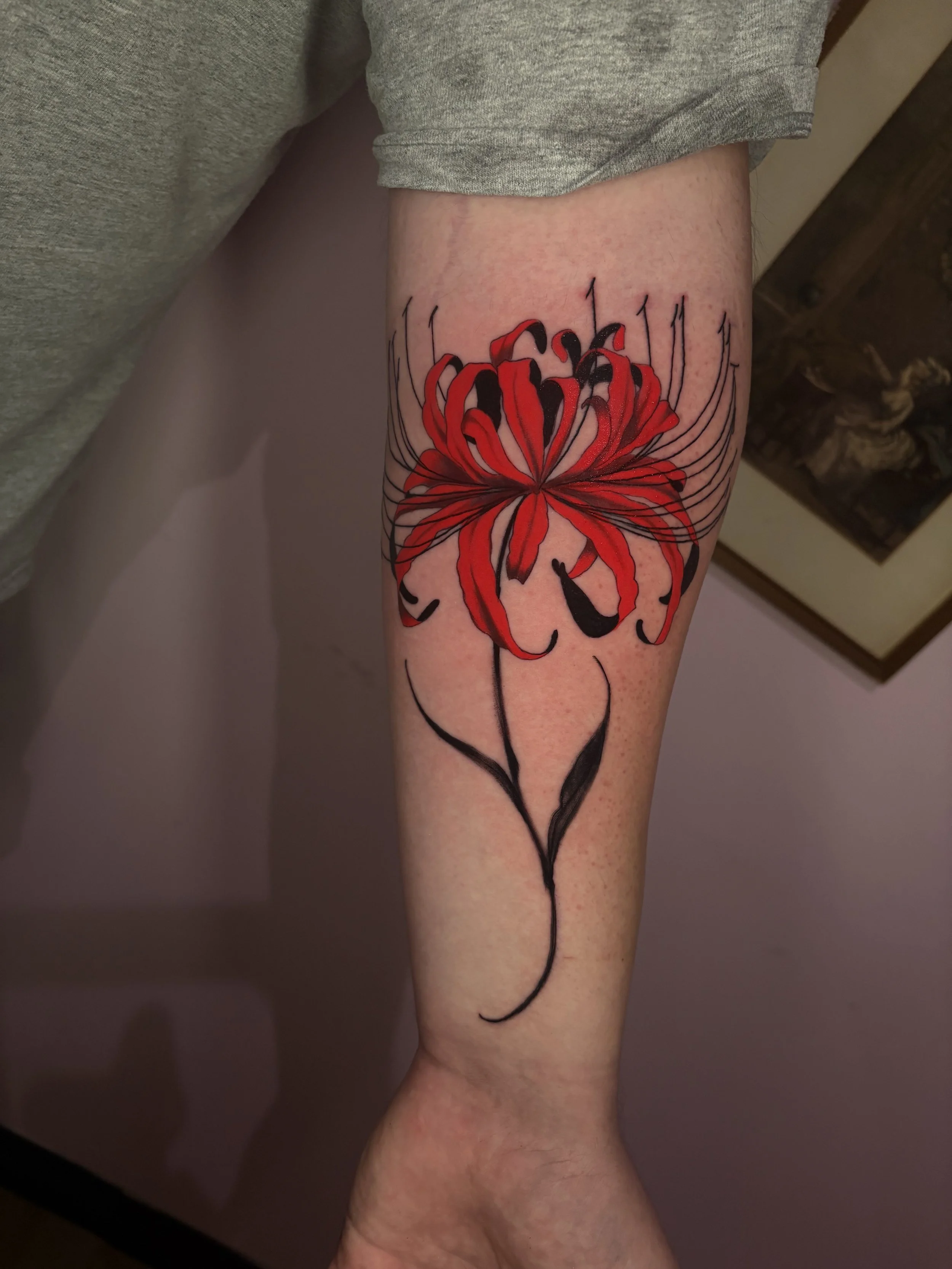 Tattoo of a red and black spider lily flower on a person's thigh.