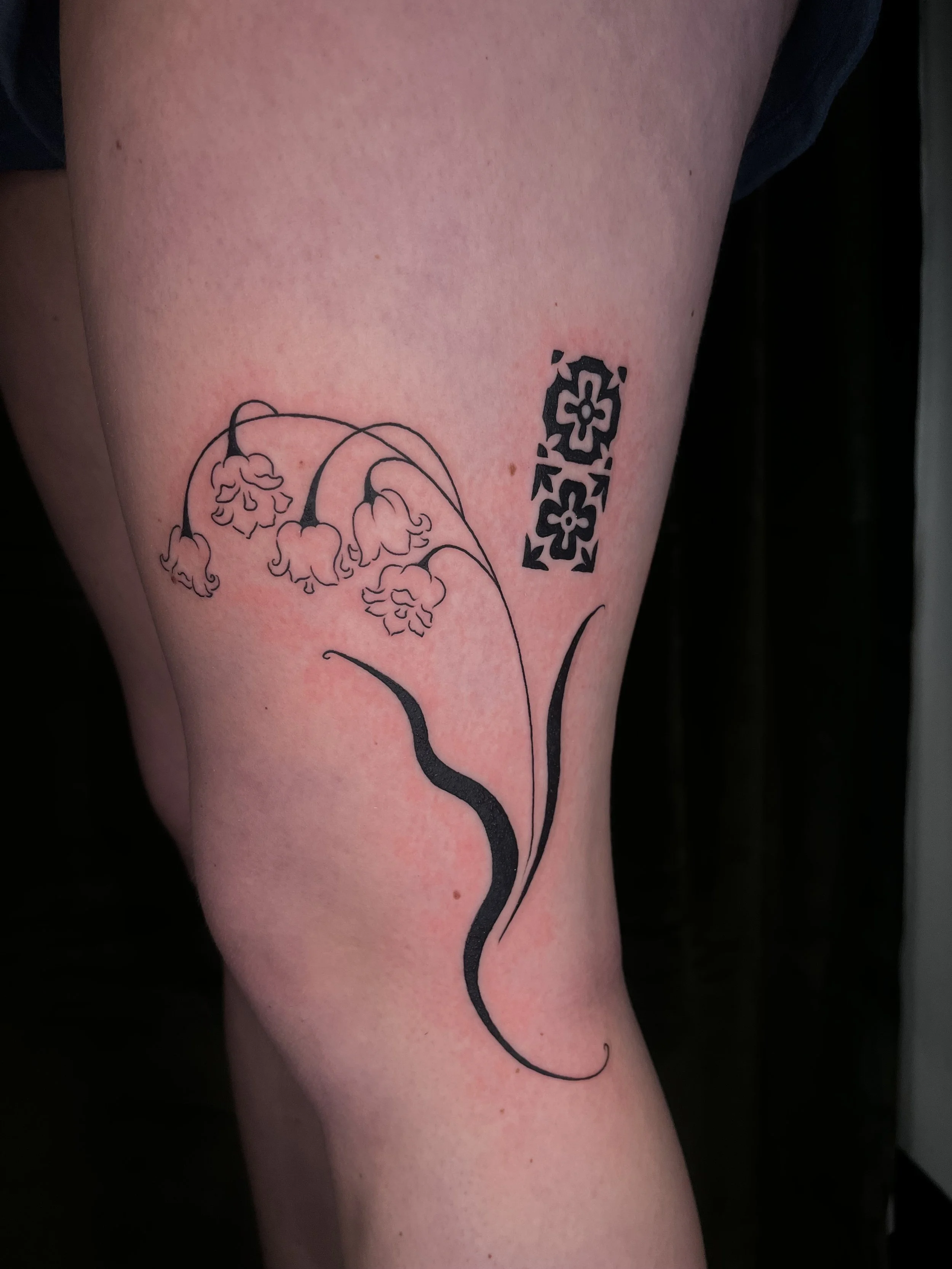 Tattoo of black floral and geometric design on a person's thigh.