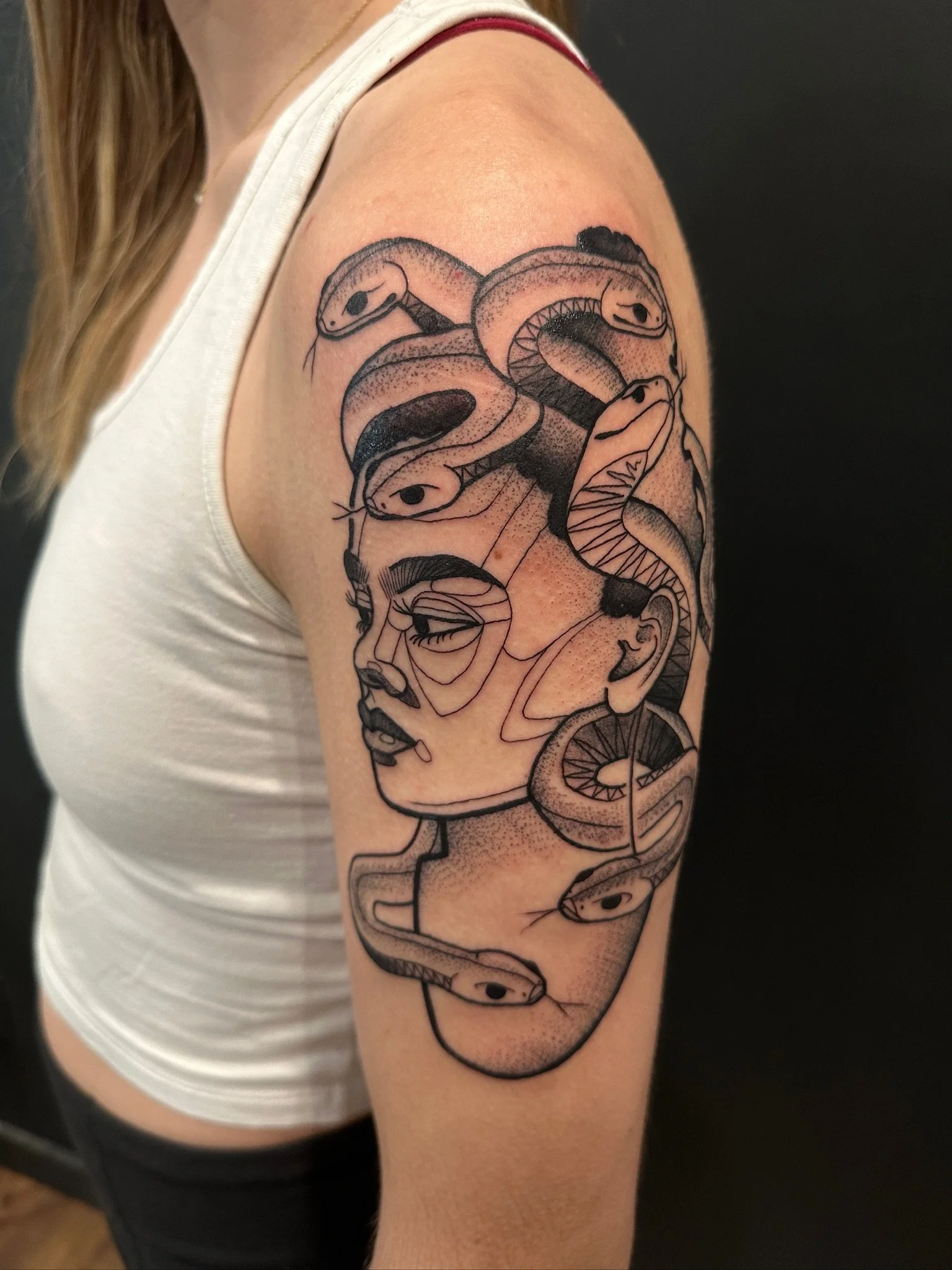 A tattoo of a snake coiled around a face on a woman's upper arm.