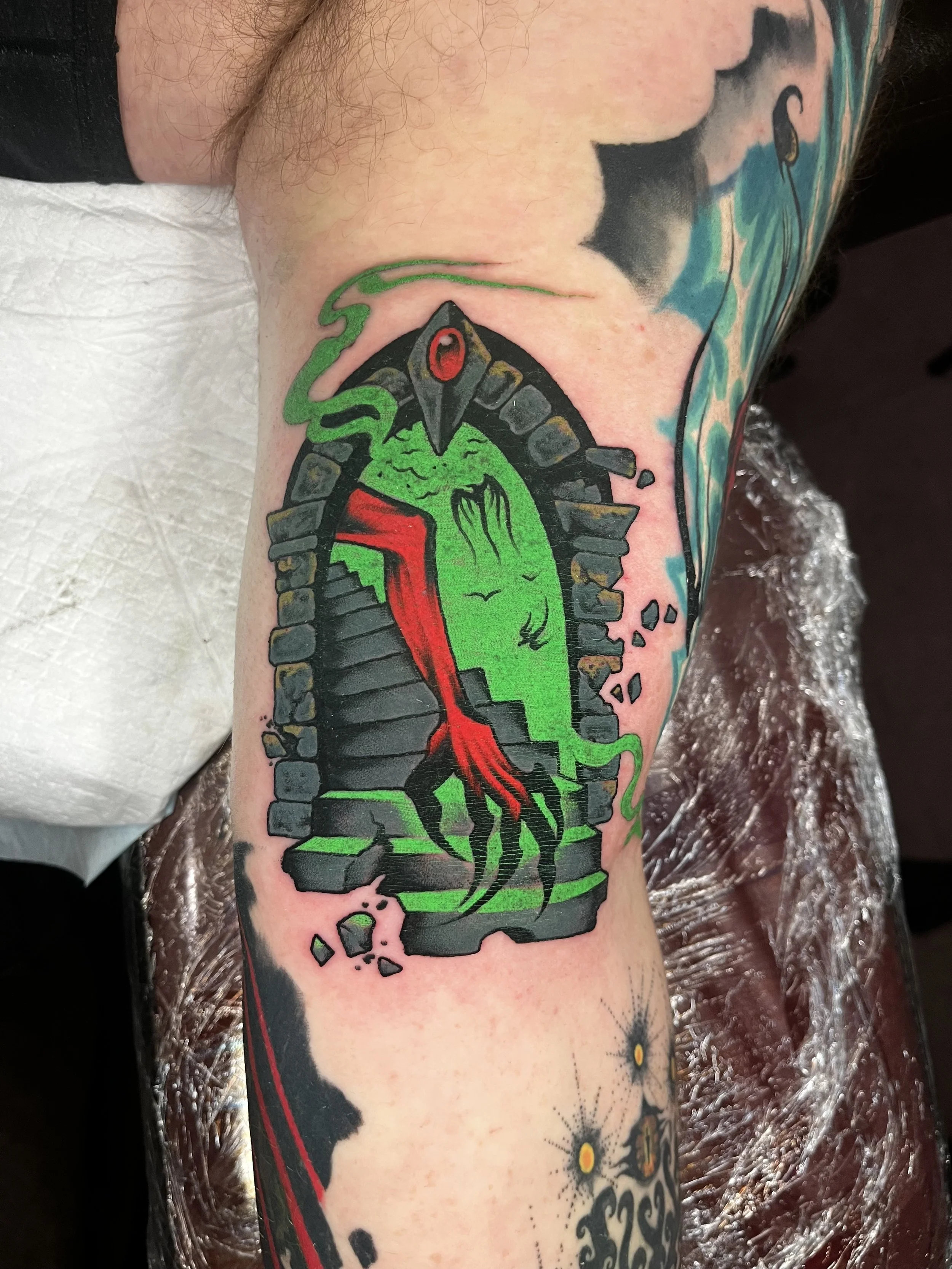Tattoo of a green gecko inside a brick doorway on a person's arm.