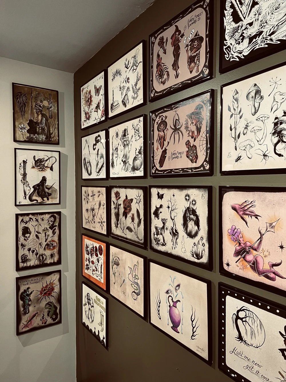 A gallery wall featuring framed illustrations of fantasy-inspired characters, creatures, and mystical themes, with a mix of black-and-white and colored artwork.