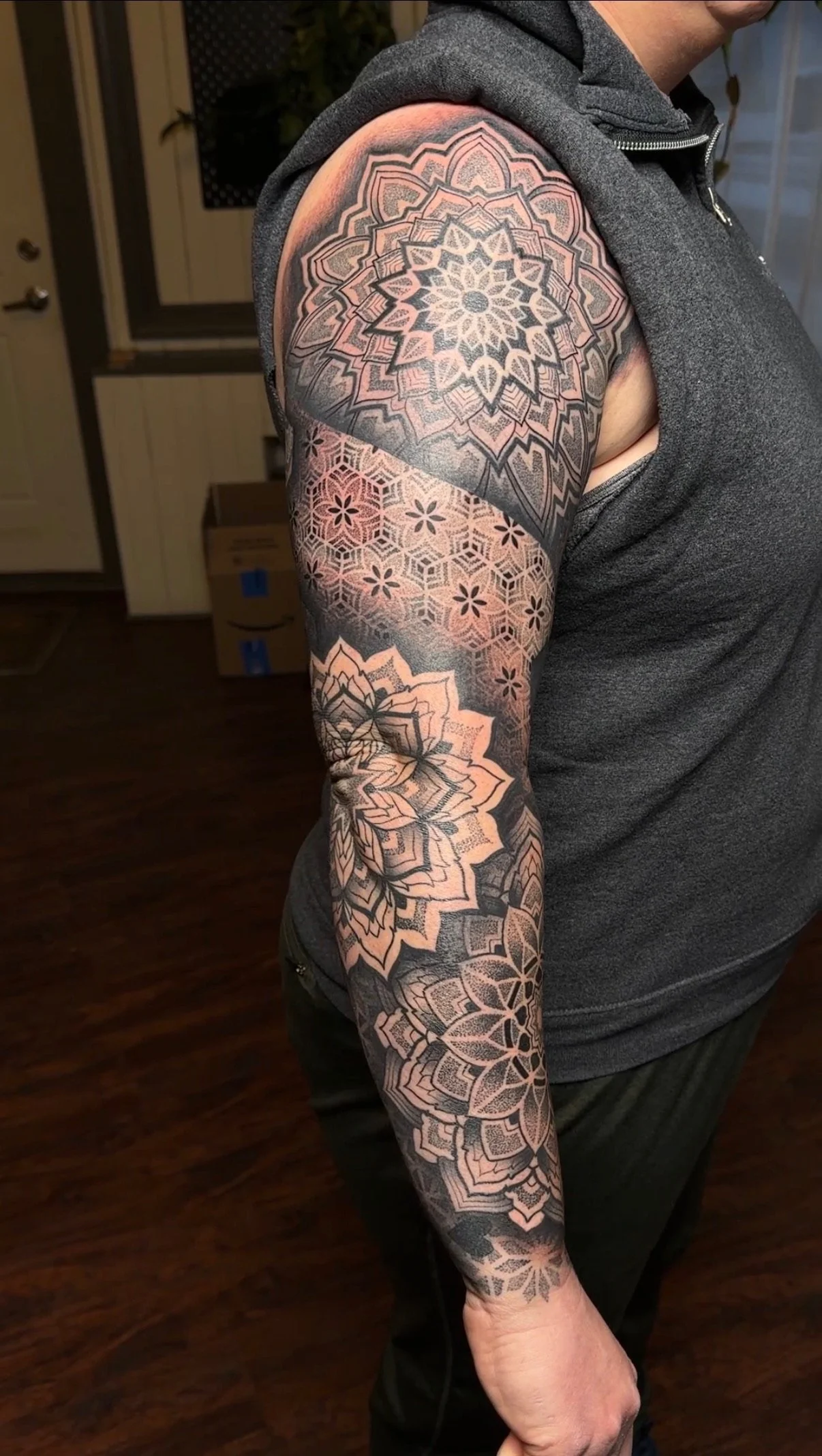 A person with a detailed black and gray geometric tattoo sleeve on their arm, featuring floral and star-like patterns.