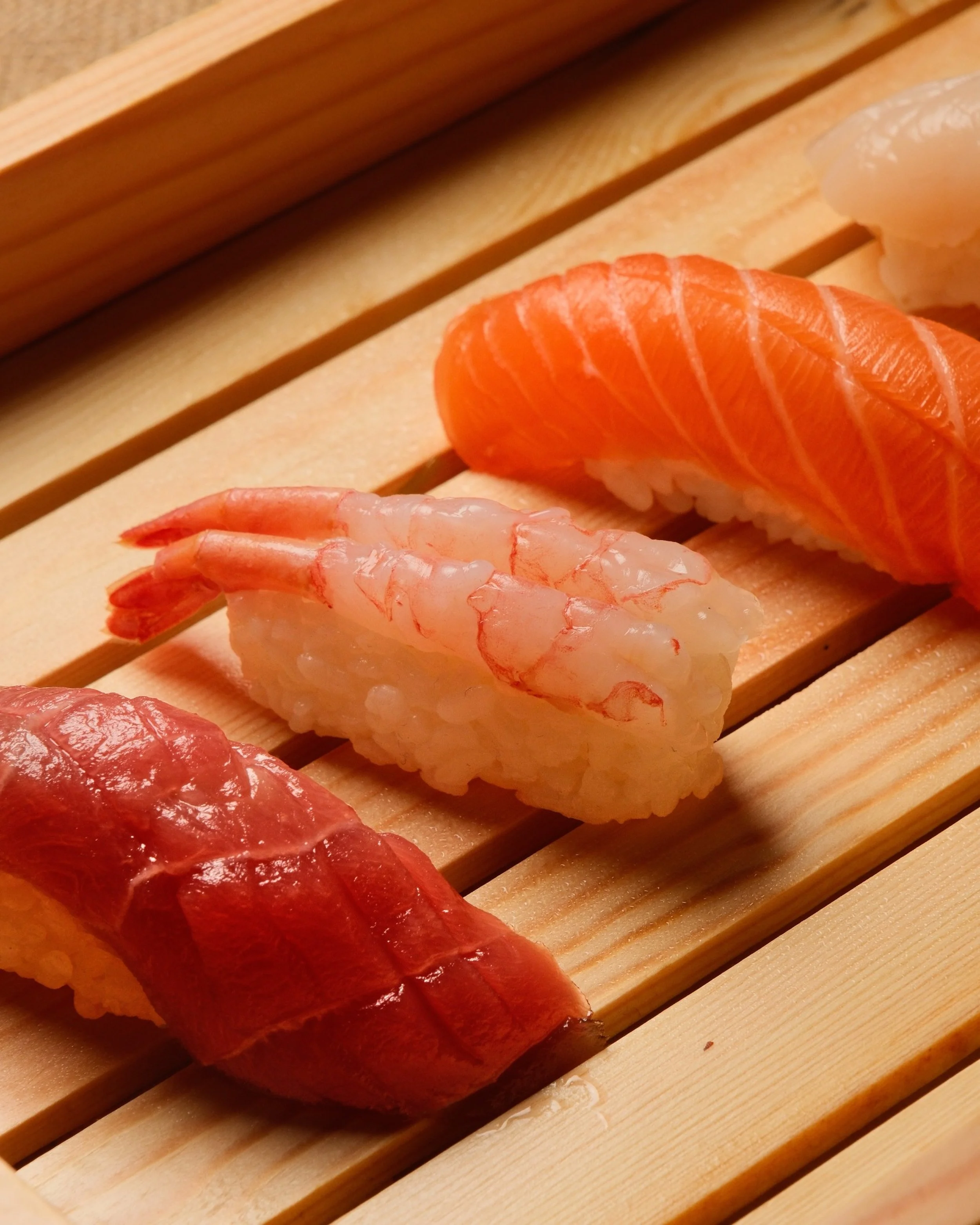 Assorted sushi pieces, including salmon, shrimp, and tuna, on a wooden sushi rolling mat.