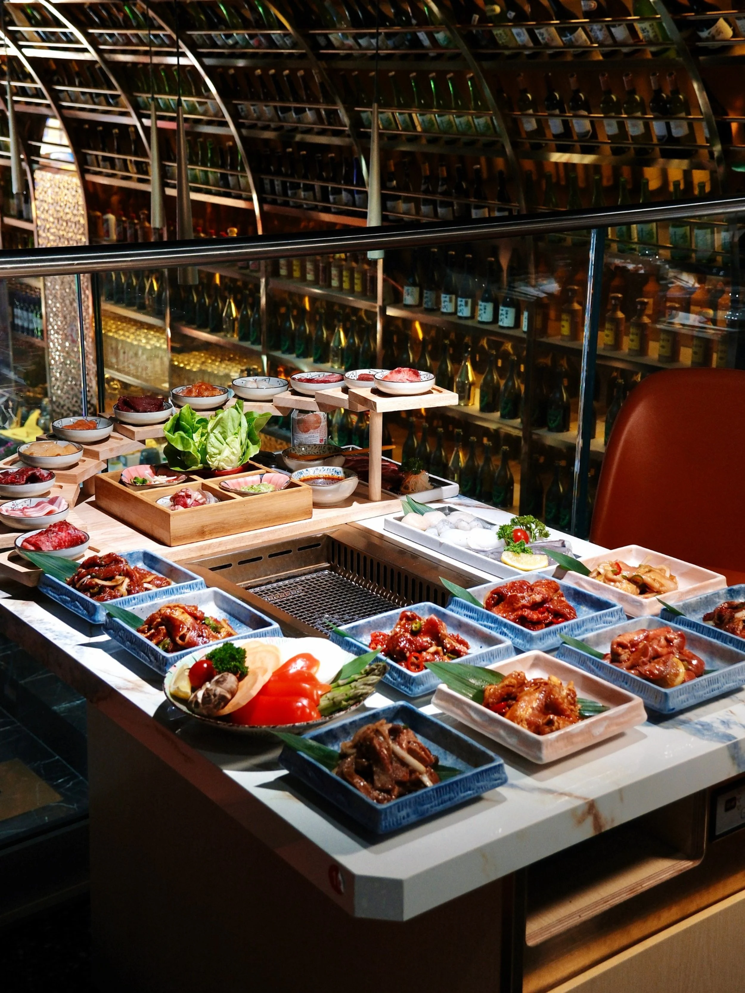 A variety of raw and cooked meats, vegetables, and sauces arranged on a table for a hot pot or Korean BBQ meal in a restaurant.