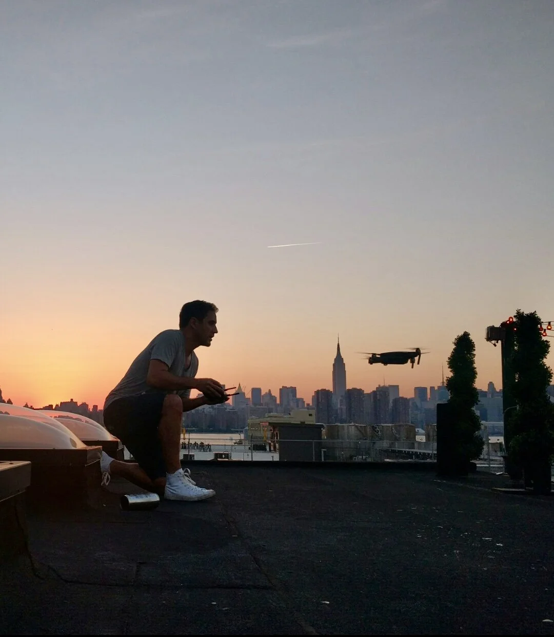 Arnaud Muller operating a drone on a rooftop above the New York skyline at sunset
