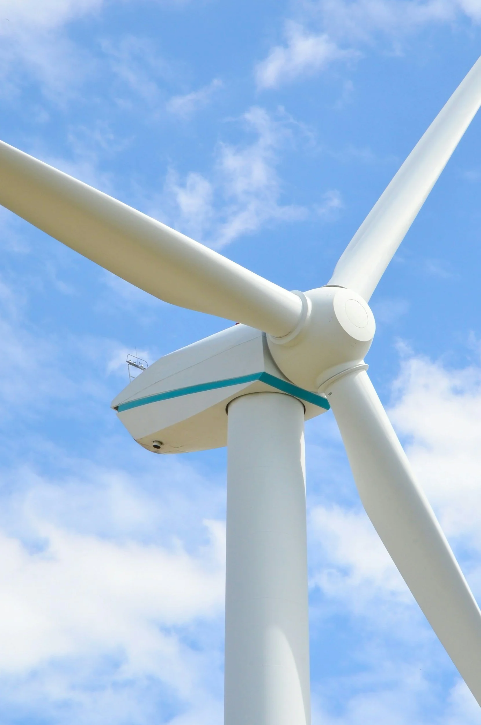 Close-up of a wind turbine against a partly cloudy blue sky.