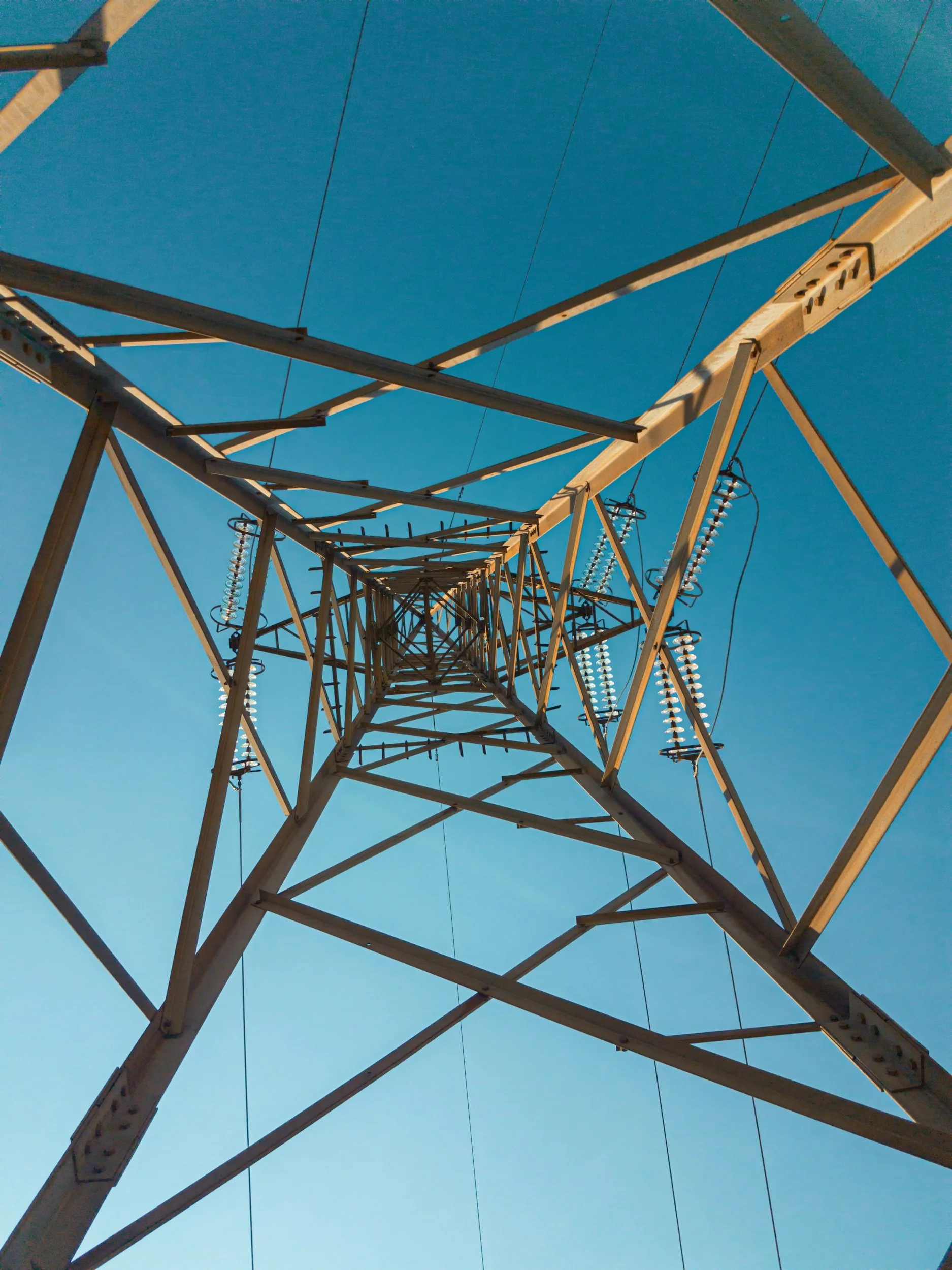 Looking up at a high voltage power tower against a blue sky.