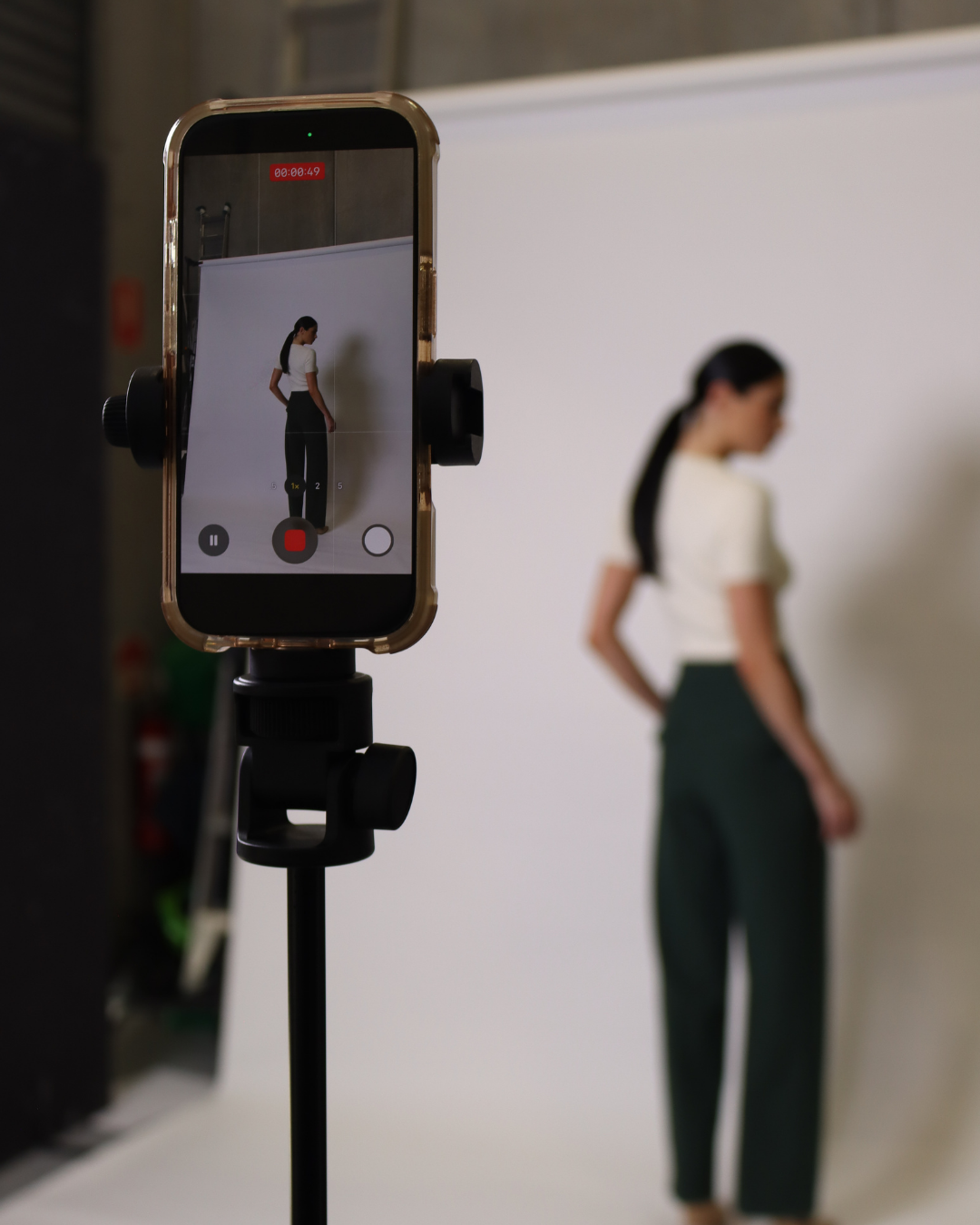 A smartphone on a tripod recording a woman standing in front of a plain white background.