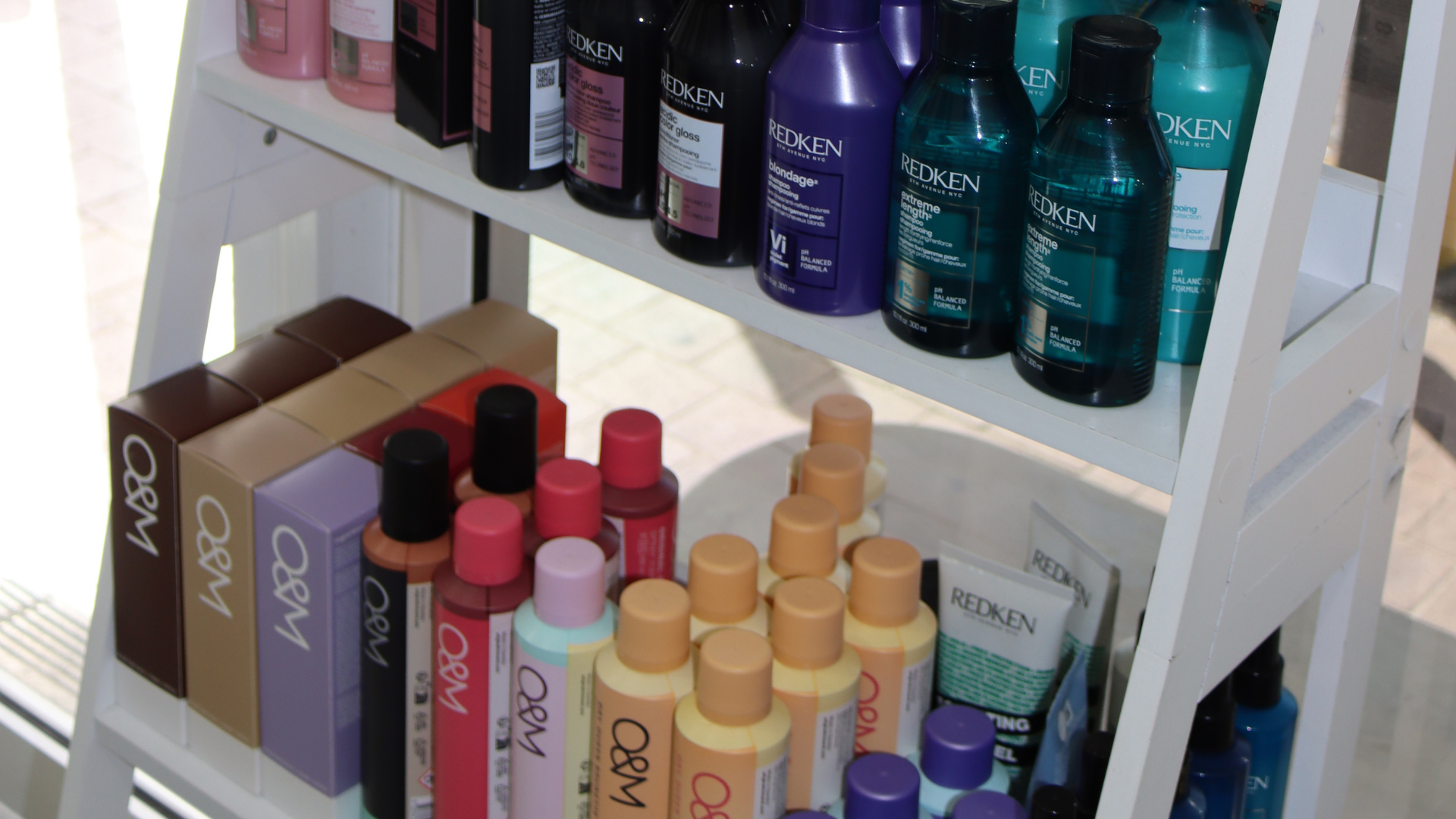 A white three-tiered shelf displaying various hair care products including shampoos, conditioners, and styling products from brands like Redken and Olaplex.