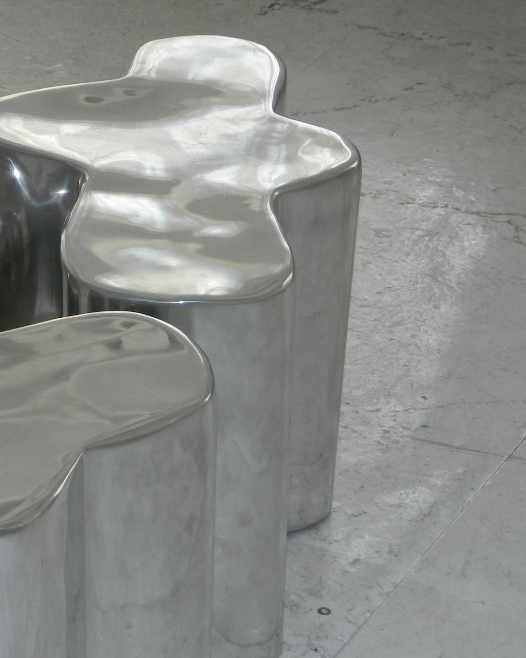 Two metallic, abstract-shaped sculptures with smooth, polished surfaces on a concrete floor.