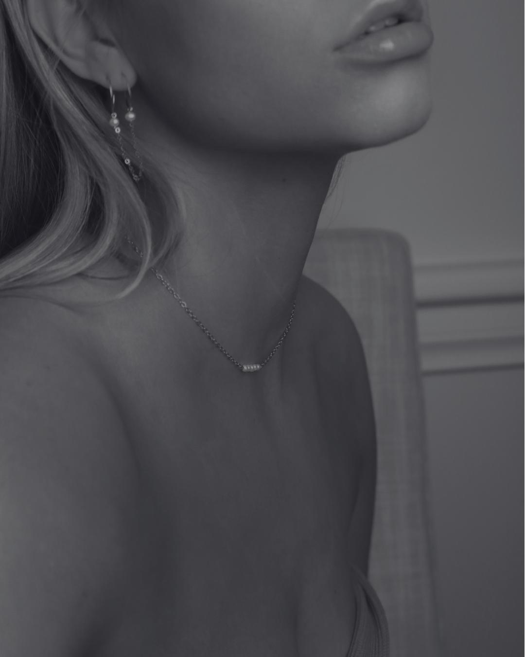 Close-up of a woman's lower face, partial neck, and shoulder, wearing earrings and a necklace, with her lips slightly parted. The photo is in black and white.