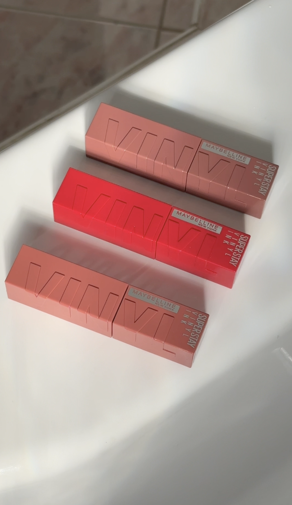 Three Maybelline SuperStay Ink lipstick boxes in different shades of pink and red, arranged on a white surface.