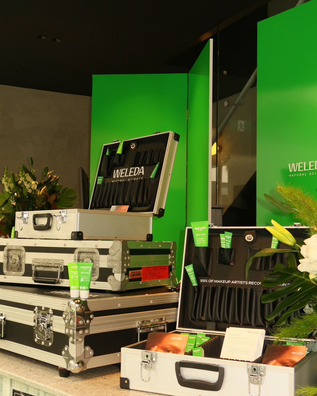 Display of Weleda skincare products, including tubes, in a professional case at an event, with green branding and floral decorations.