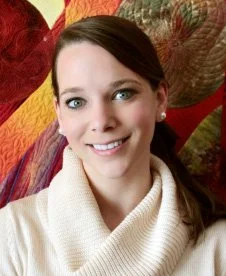 A woman smiling for a portrait, wearing a white turtleneck sweater, with a colorful abstract background.