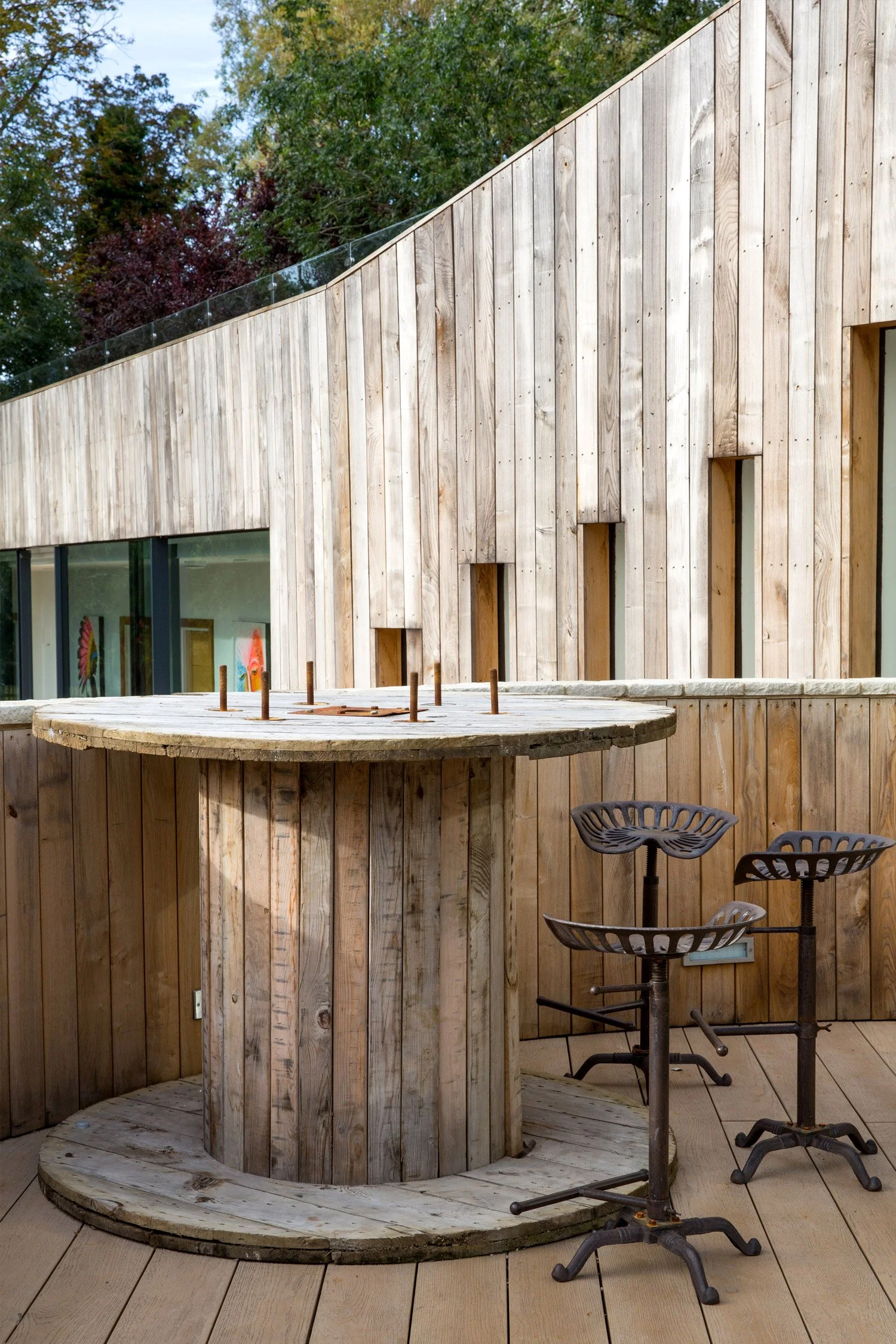 A modern exterior building with wooden paneling and a large outdoor bar area with high metal stools.