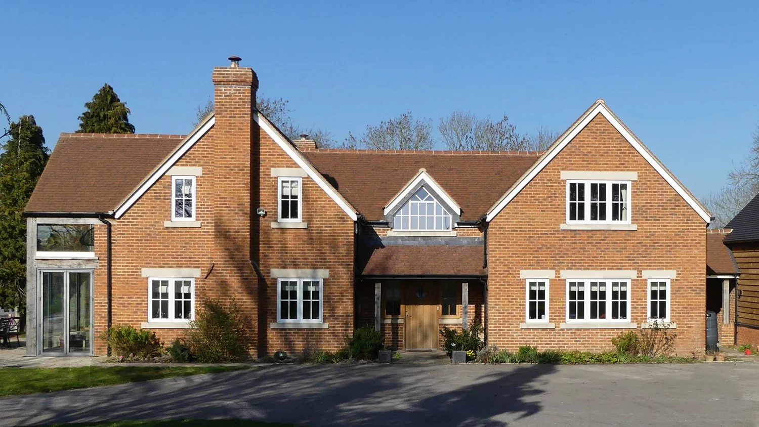 A large brick house with multiple gabled roofs, white window frames, and a central wooden door, set against a clear blue sky.