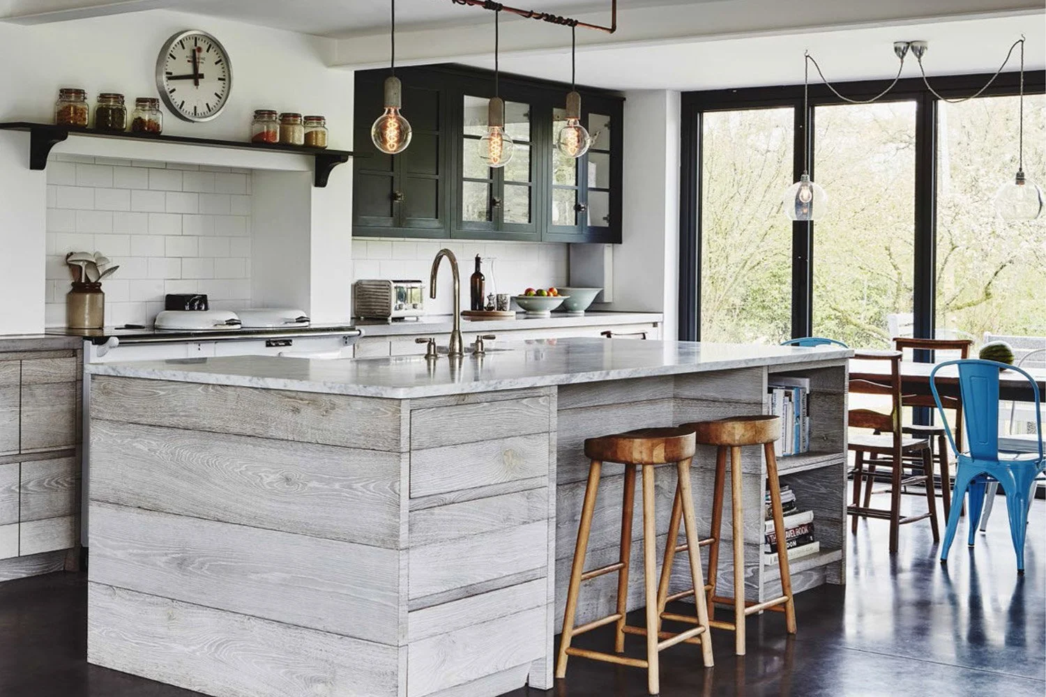Modern kitchen with a large island, gray and white cabinets, large window, and hanging light bulbs.