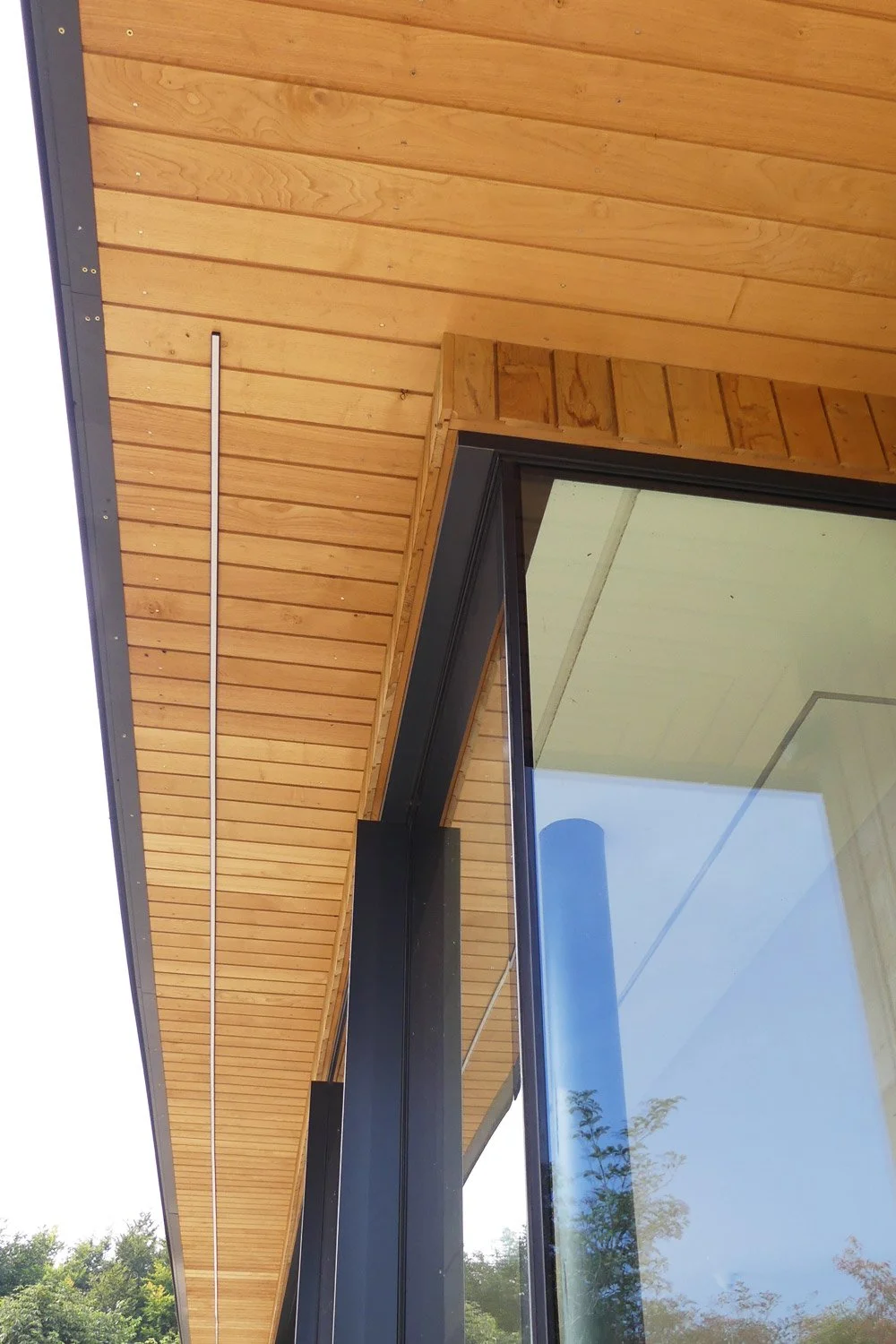 Close-up of a modern building corner with wooden siding, large black-framed glass windows, and metal trim in an outdoor setting.