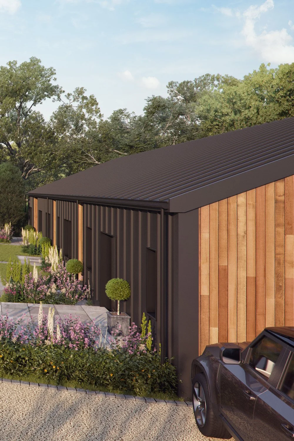 A modern building with wooden and black exterior walls, surrounded by a landscaped garden with flowering plants and trees, under a blue sky.