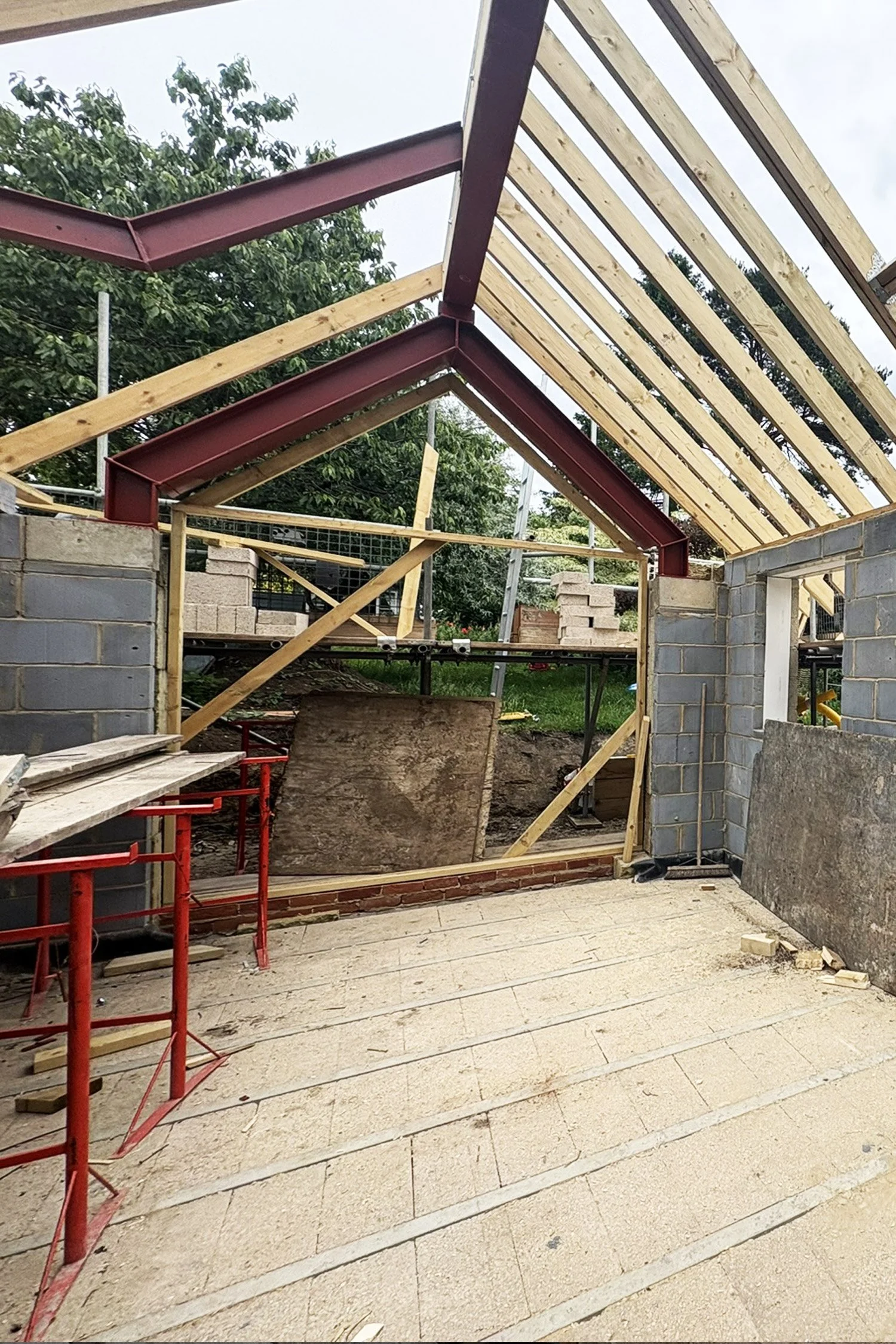 Construction site with a partially built structure, showing brick walls and wooden roof framework.