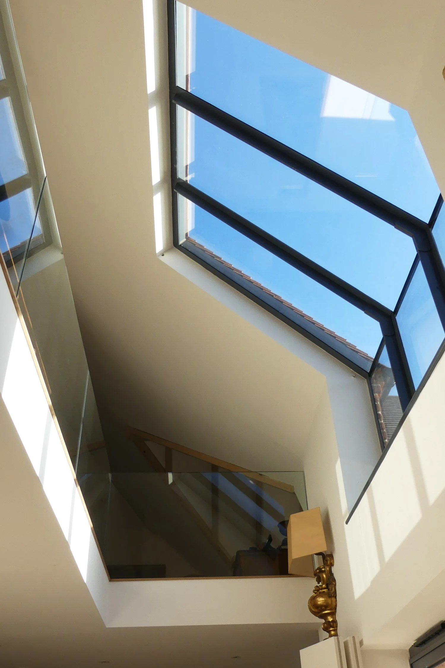 View of a bright blue sky through a large, open skylight in a modern interior space.